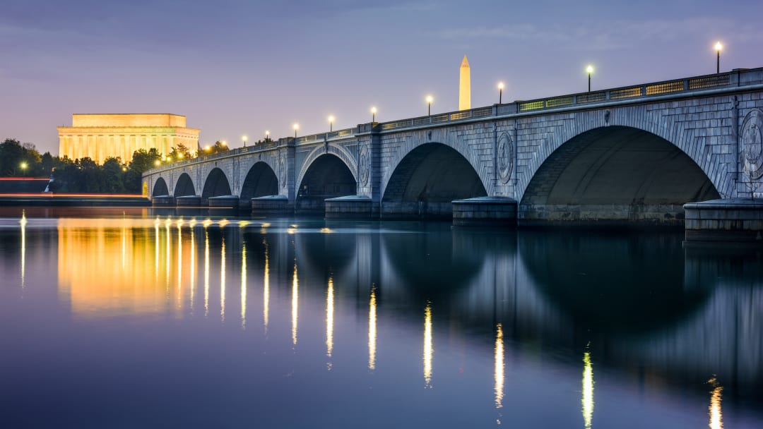View of the Arlington Memorial Bridge at dusk. The Lincoln Memorial and the Washington Memorial appear in the background. 