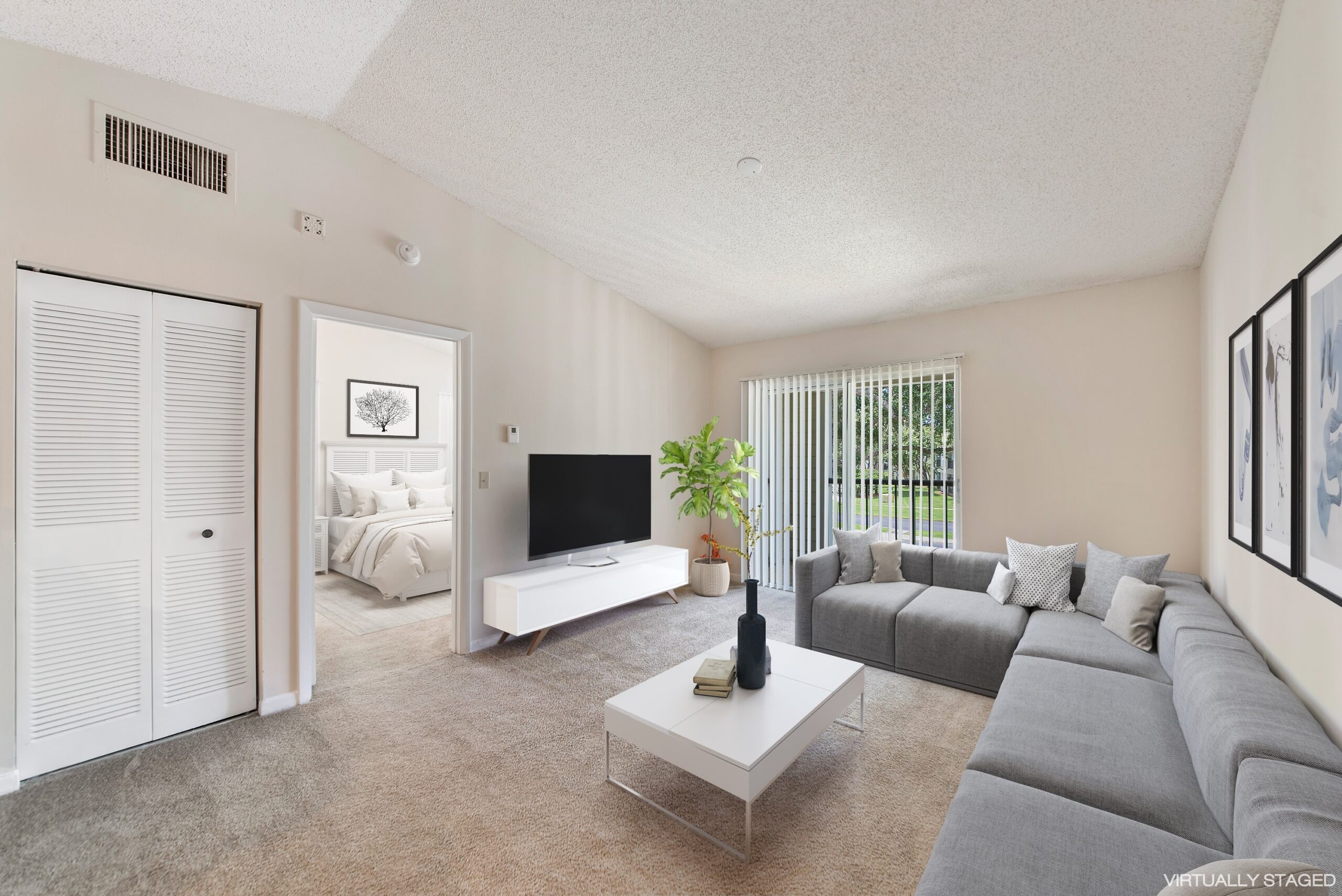 Living room with grey sectional sofa and flat screen tv. Sliding glass door to outdoor patio. There is also a view into the bedroom.