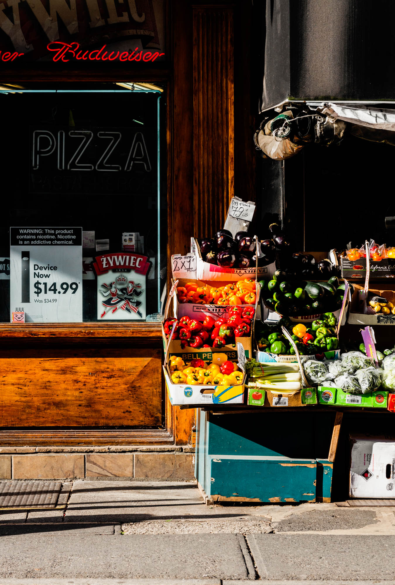 An outdoor produce stand next to a shop offering pizza and beer in Greenpoint Landing near Two Blue Slip apartments.