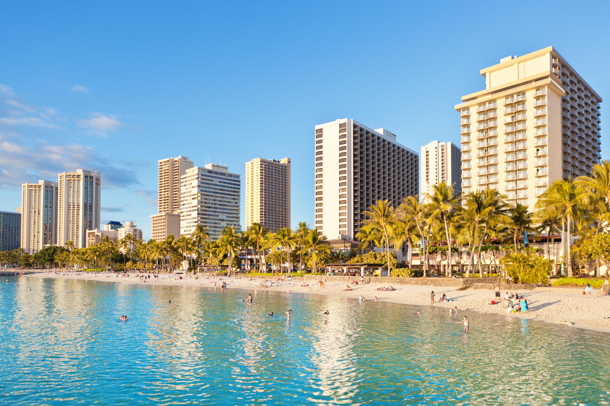 Waikiki Beach busy with sunbathers and tourists, with resort hotel in the background.