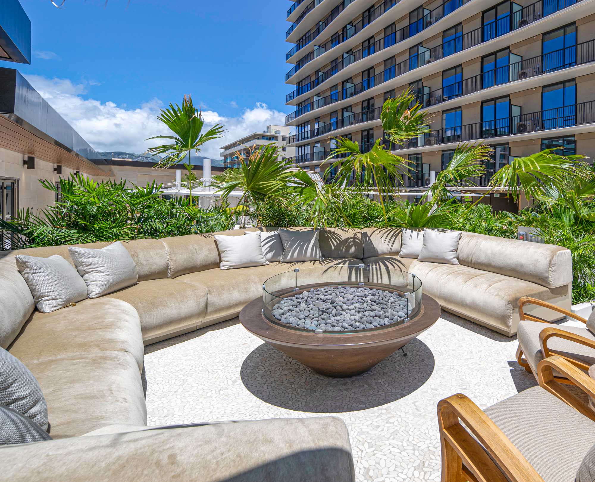 Plush outdoor seating around a fire pit surrounded by palm trees.