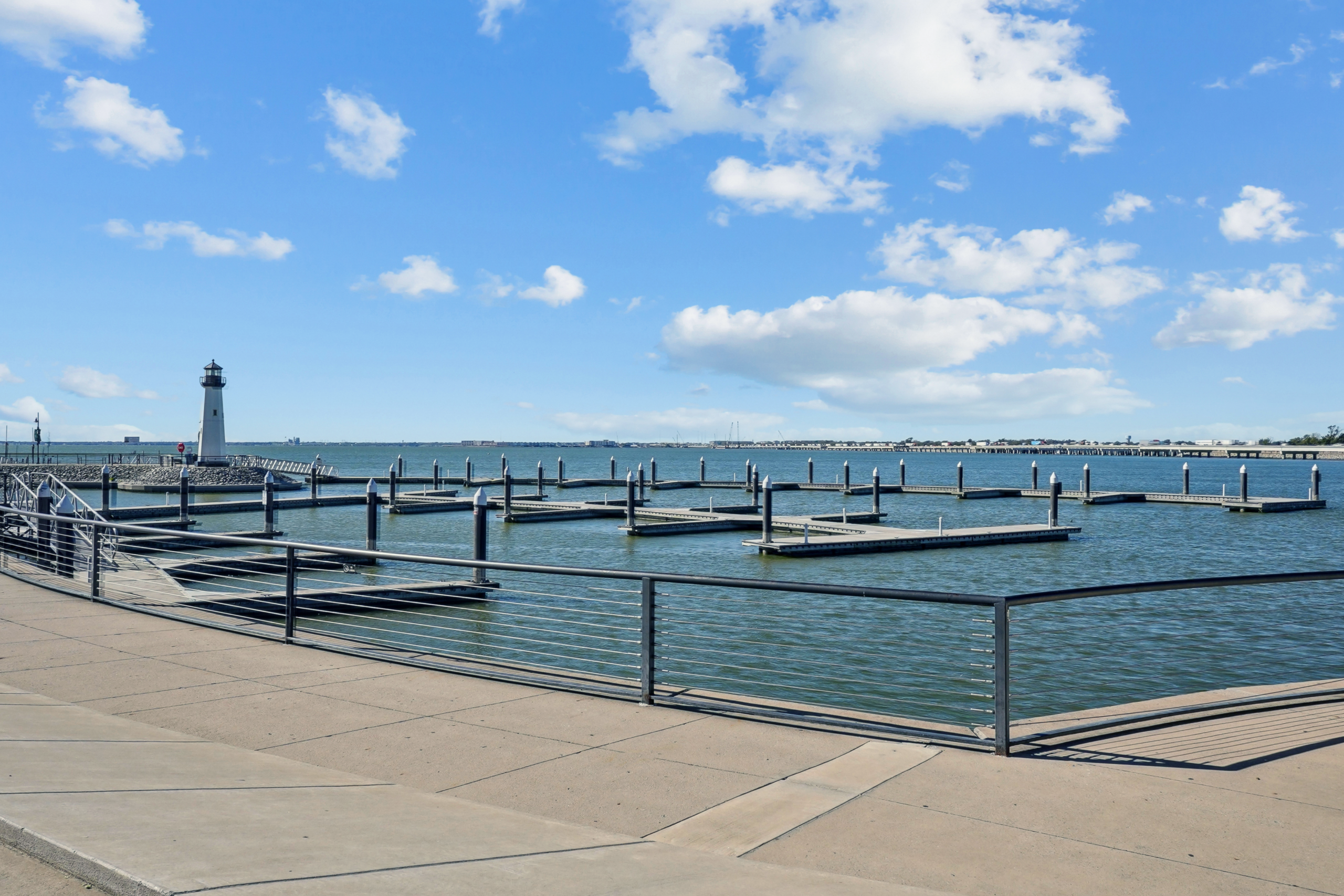 Waterfront marina with empty boat slips and a lighthouse under a bright blue sky near Embree Hill apartments in Garland, Texas