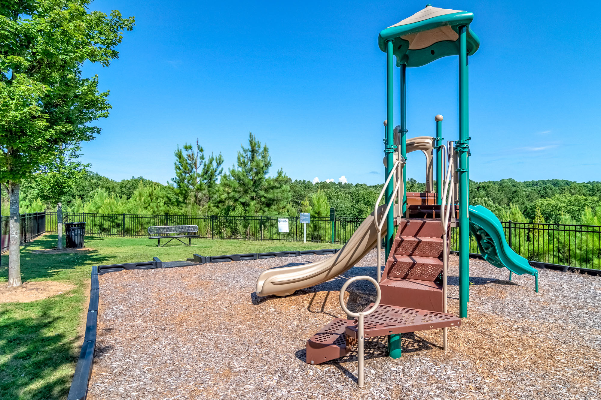 A fenced in playground is surrounded by trees at Park 9 apartments in Woodstock, GA.