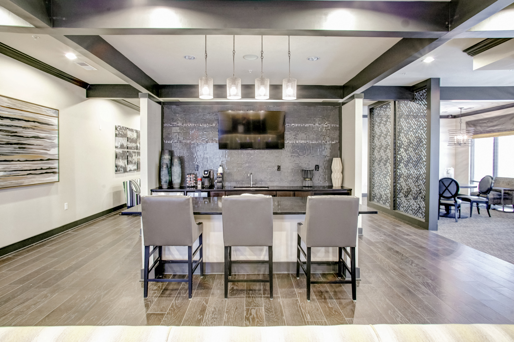 Three bar stools sit against a kitchen island. In the background is a coffee maker, sink, and a television mounted to the wall.