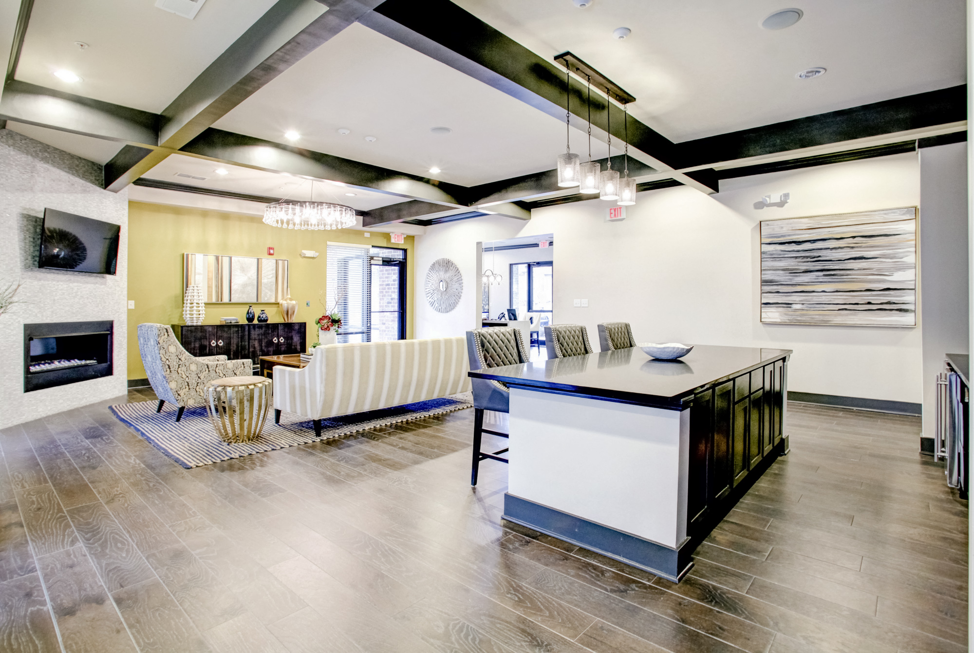 A large kitchen island is surrounded by three bar stools. In the background is a seating area with a tv and fireplace.