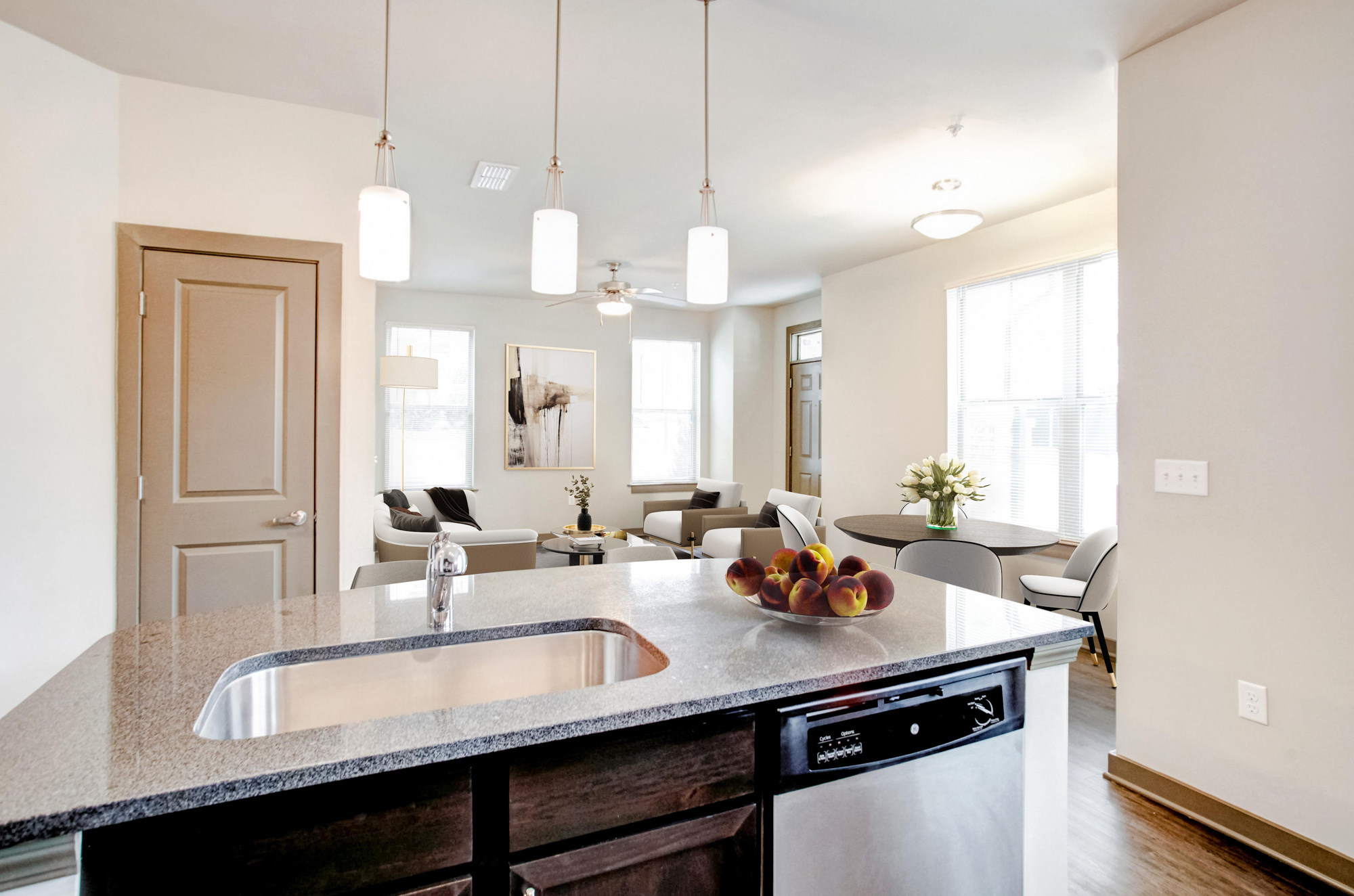 A kitchen island with peaches sitting on top is in the foreground with a seating area and kitchen table in the background.