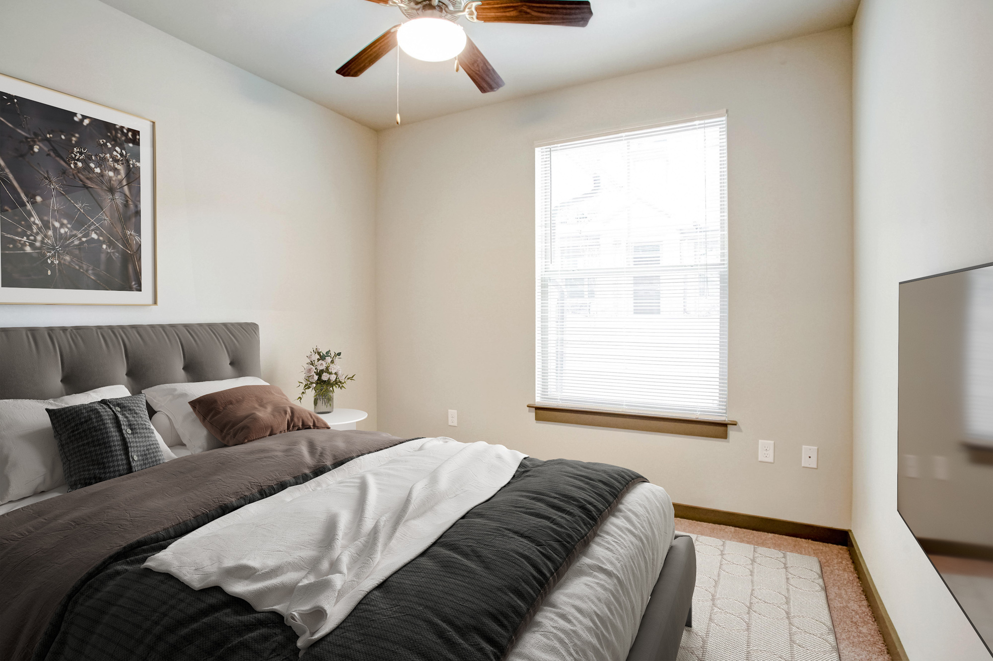 A bed with a brown comforter sits in the foreground with a picture window in the background.