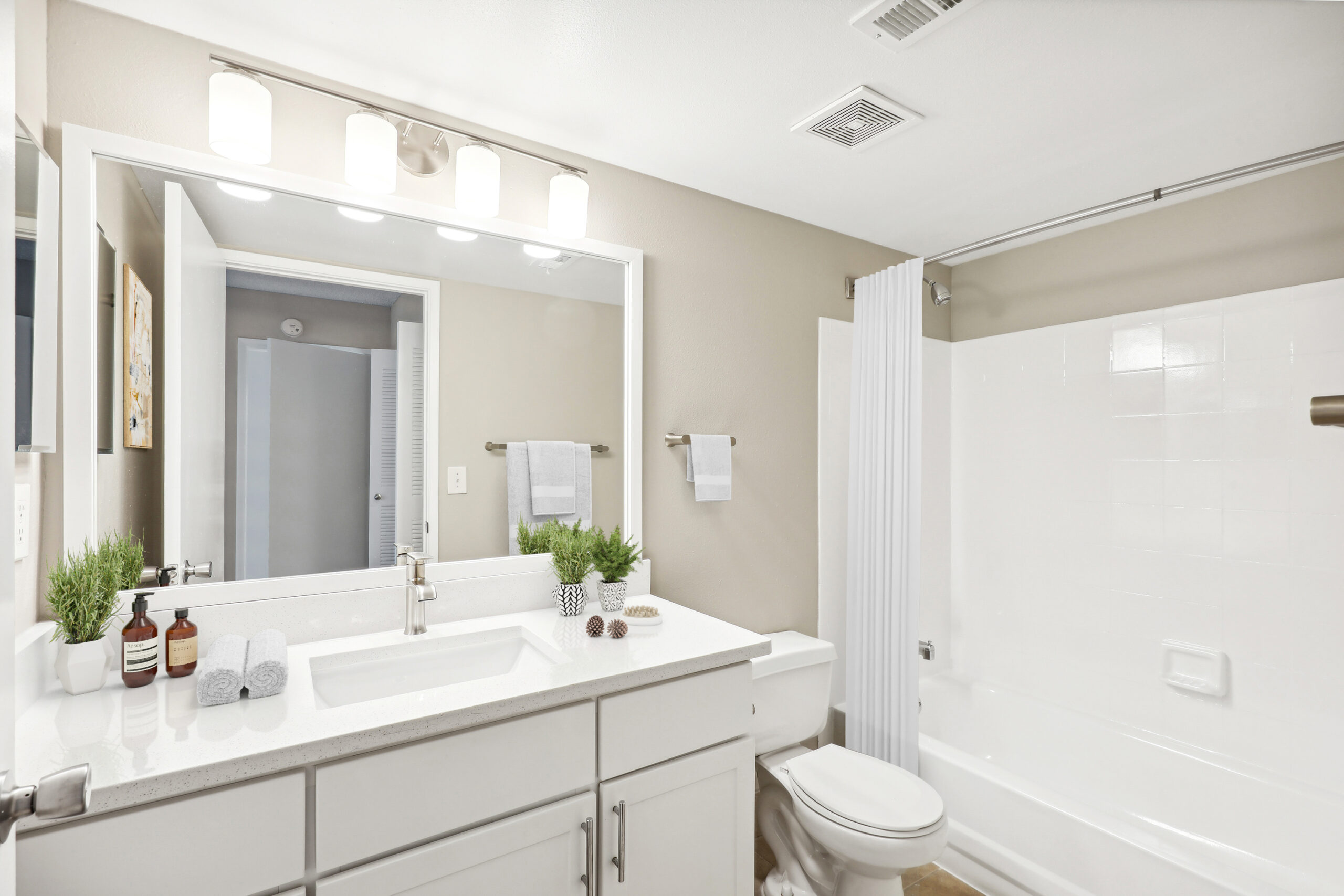 Bathroom renovation with white vanity, large mirrow with 4 vanity lights, bathtub shower combo.