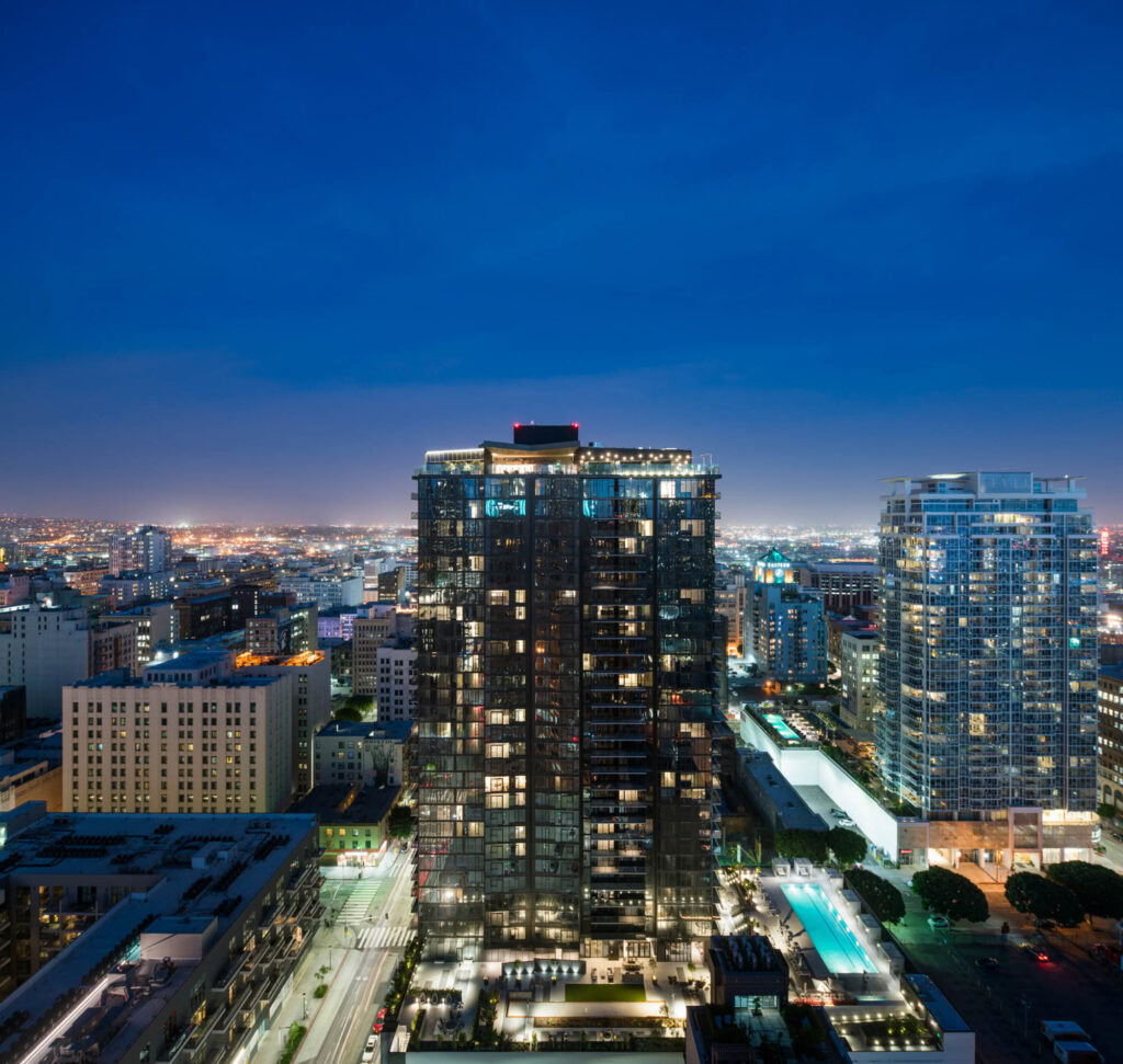 A rooftop level exterior image of the Atelier apartment building with vibrant buildings and the evening city skyline in downtown LA