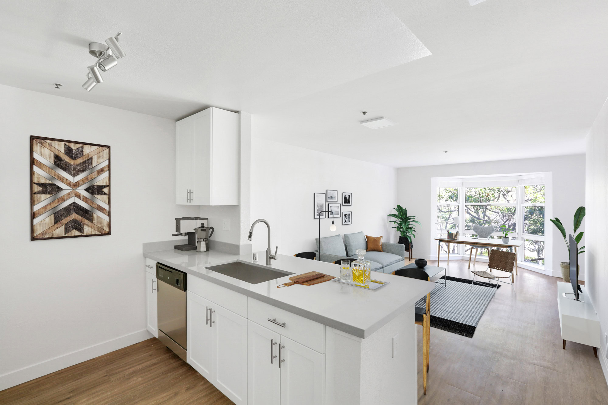 A kitchen peninsula with a sink facing a living room with a large bay window at Bayside Village apartments in San Francisco