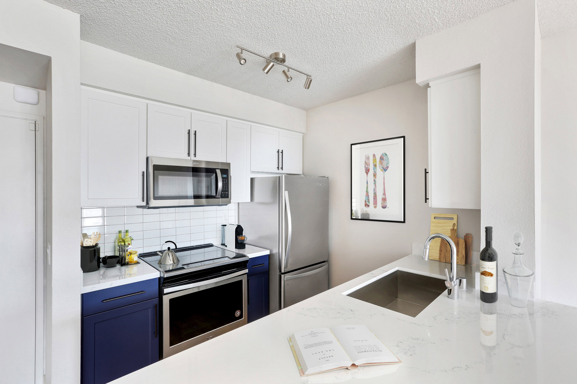 A kitchen with blue and white cabinets and stainless steel appliances in a Bayside Village apartments in downtown San Francisco