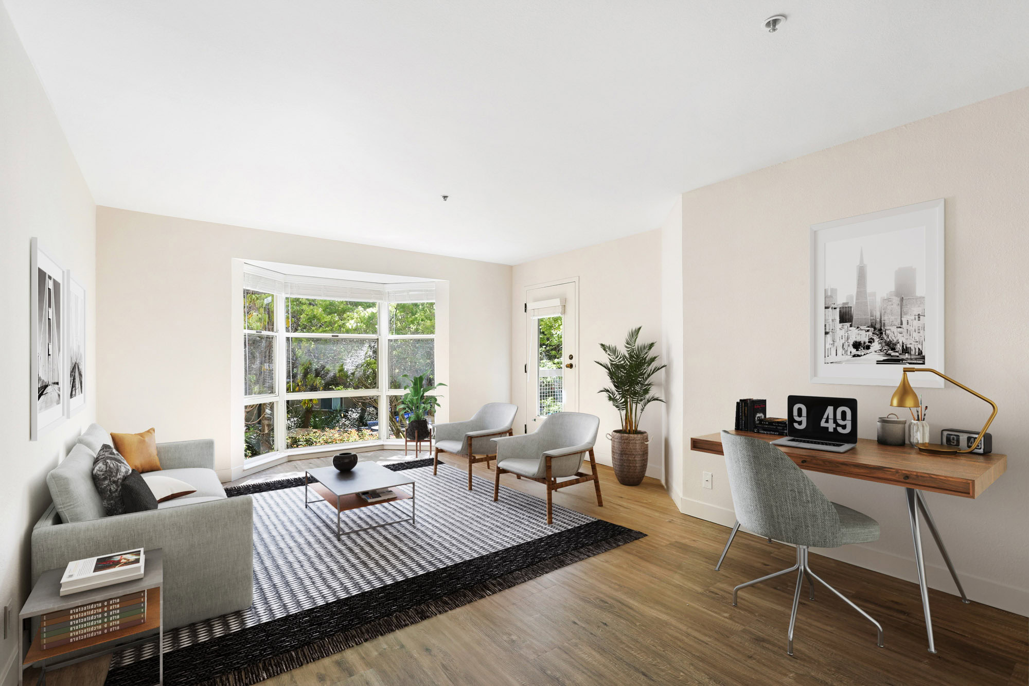 A spacious living room with a large bay window, work space and hardwood flooring at Bayside Village apartments in San Francisco