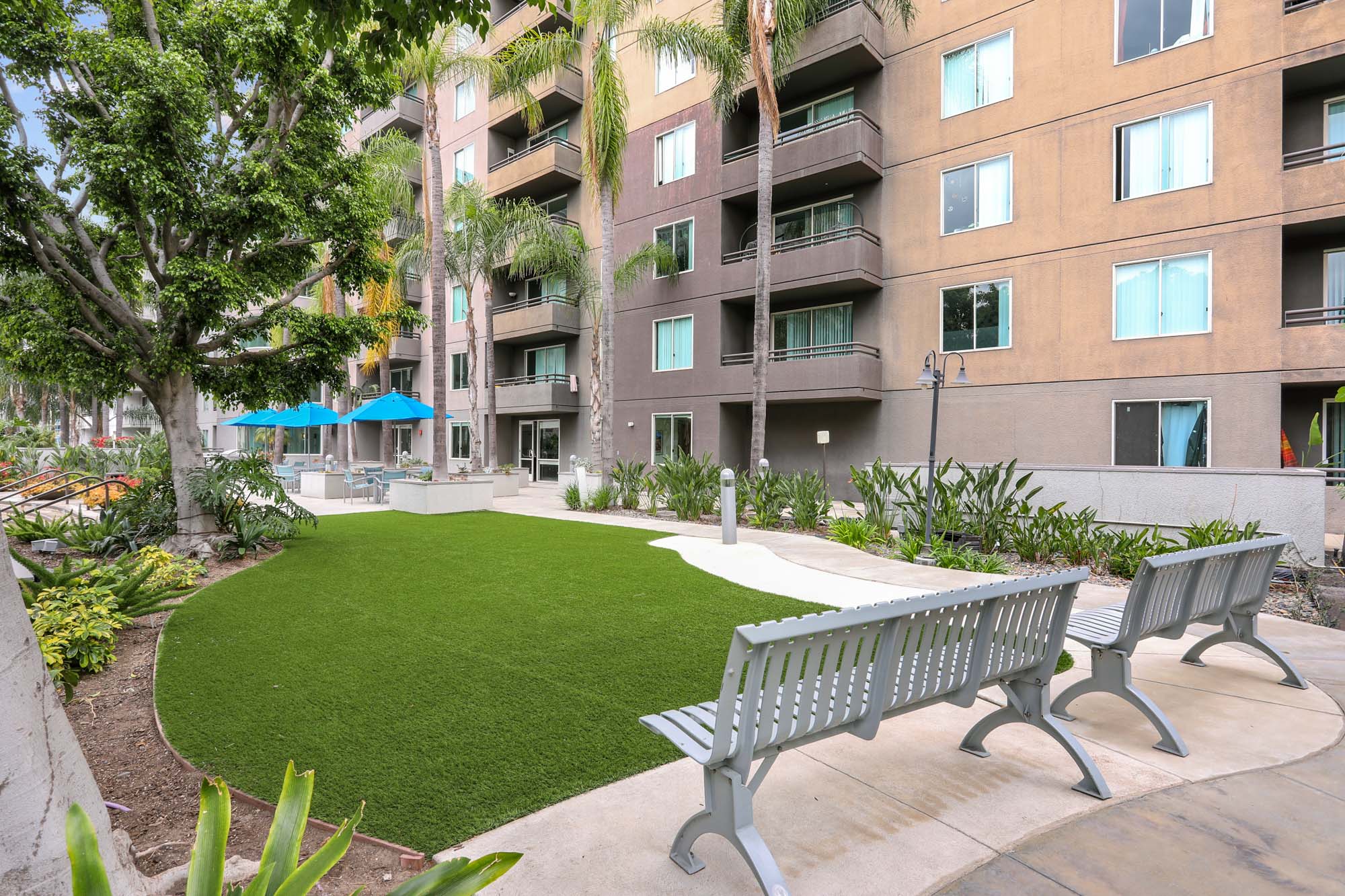 An outdoor courtyard with manicured grass and bench chairs next to the Mets modern apartments in downtown LA