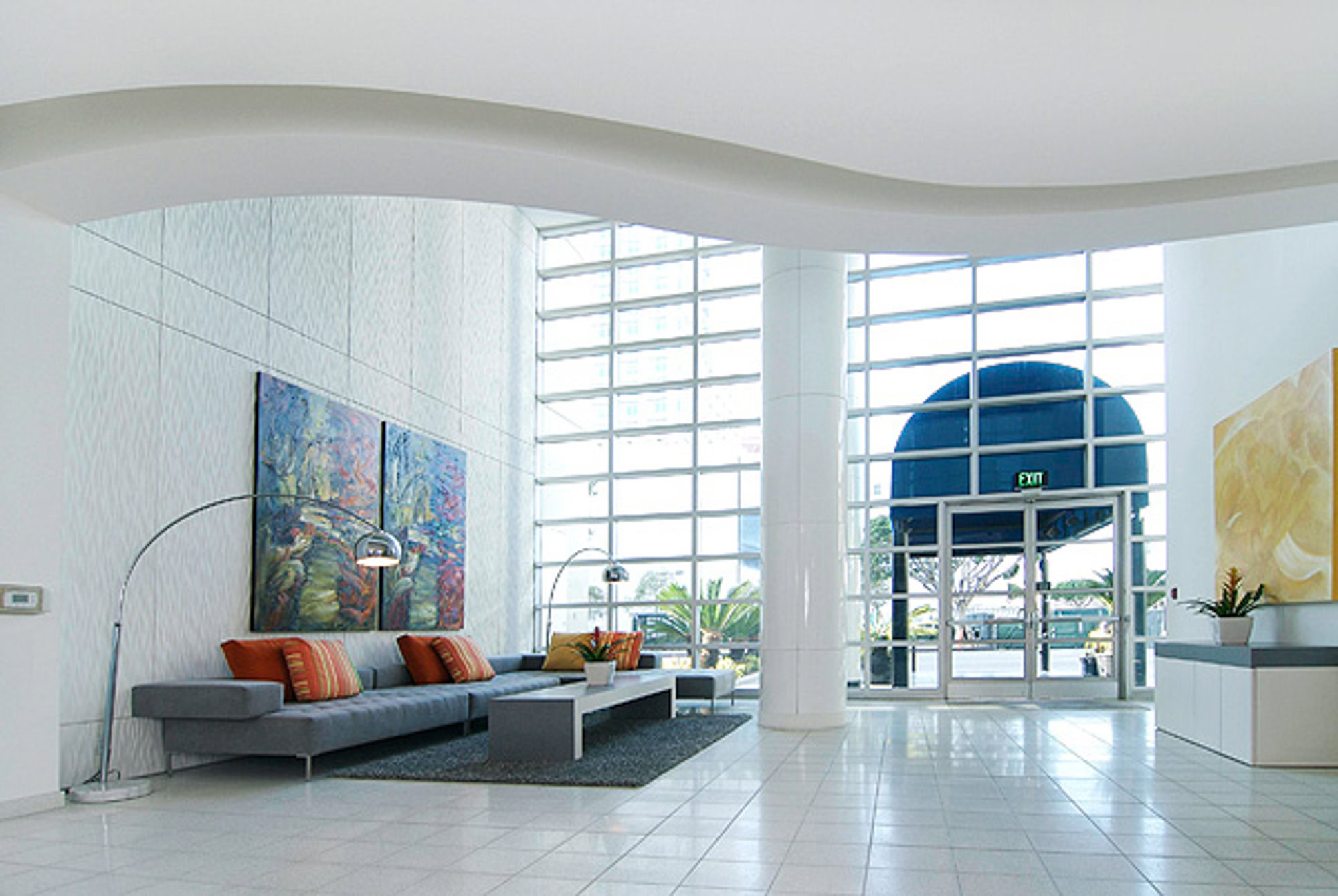 A modern spacious lobby area with a large floor to ceiling window wall and couch in front of the front desk at The Met apartments in DTLA