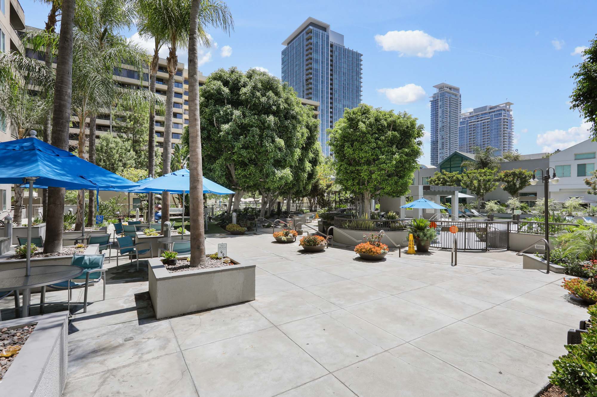A pool area with lounging chairs and tables, umbrellas and trees at The Met apartments in downtown LA