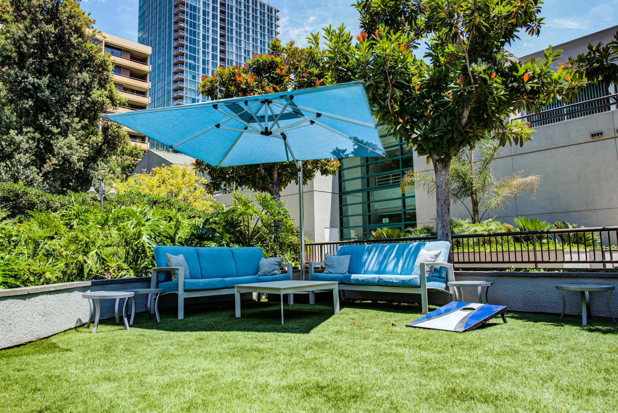 A pool seating area with an umbrella on the grass, next to a cornhole at The Met apartments in downtown LA