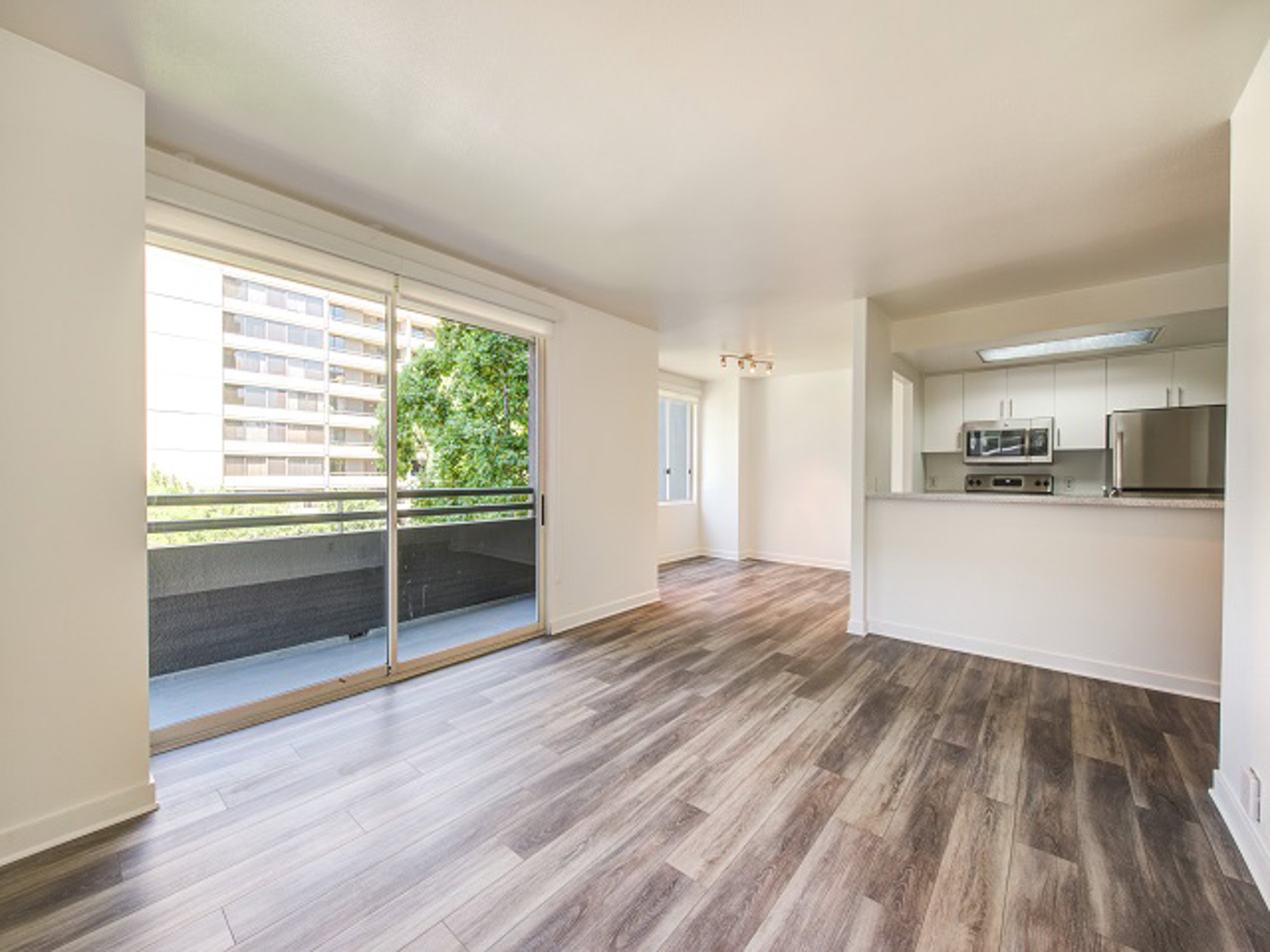 An empty apartment with an open plan living room, a den space, and a sliding door to a balcony at The Met in downtown LA