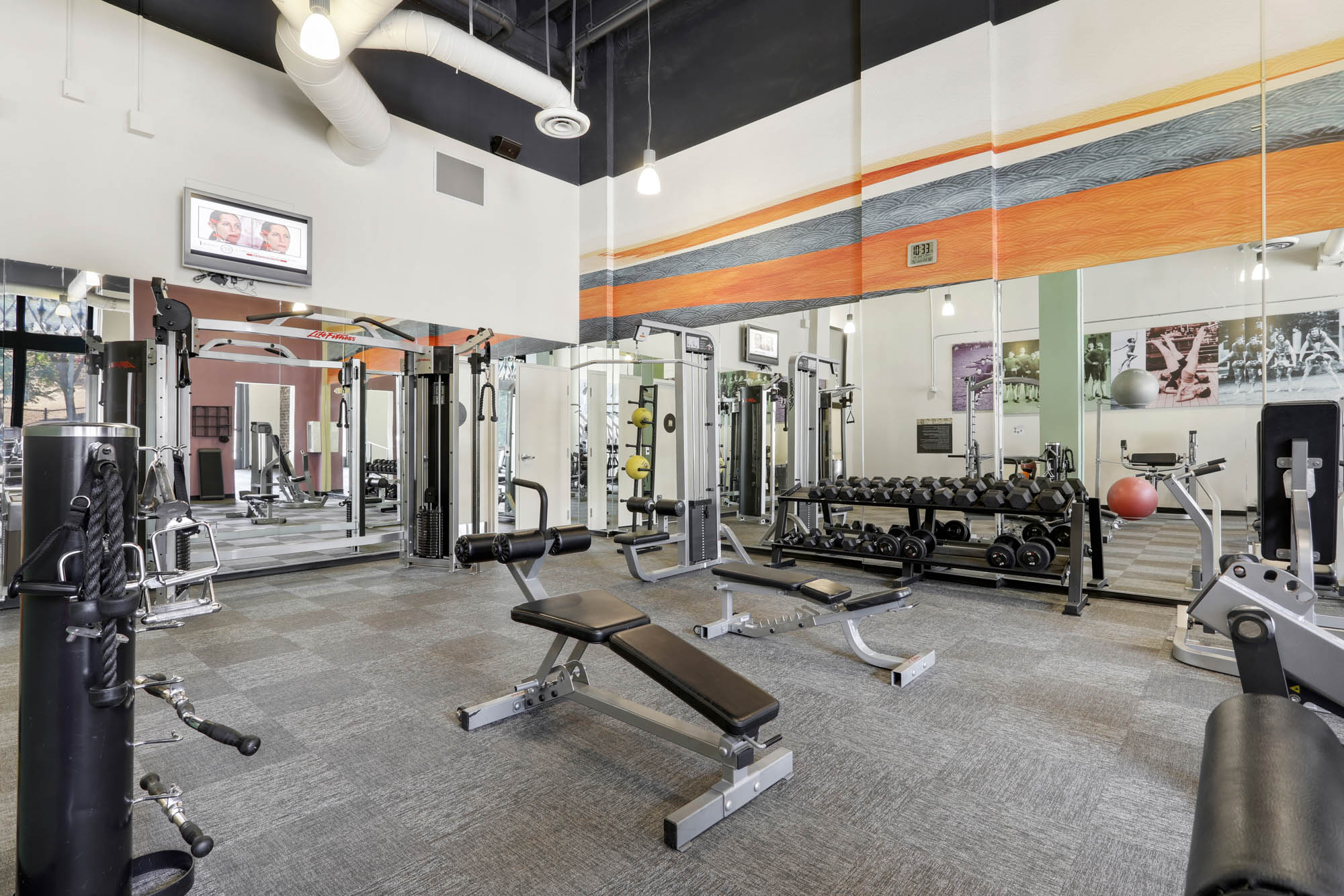 A fitness center with free weights, cardio machines and mirror on the wall.