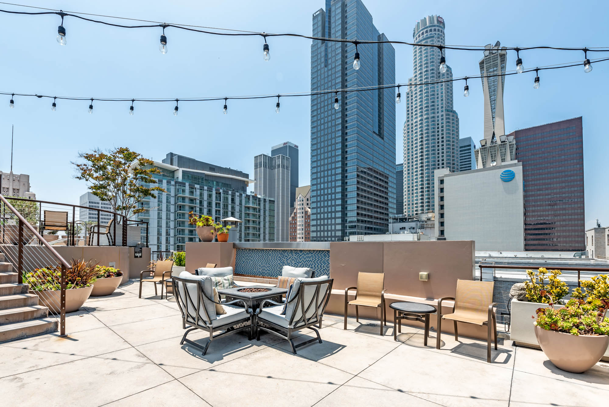 A rooftop lounging area with chairs surrounding a fireplace with city views at Metro 417 apartments in downtown LA