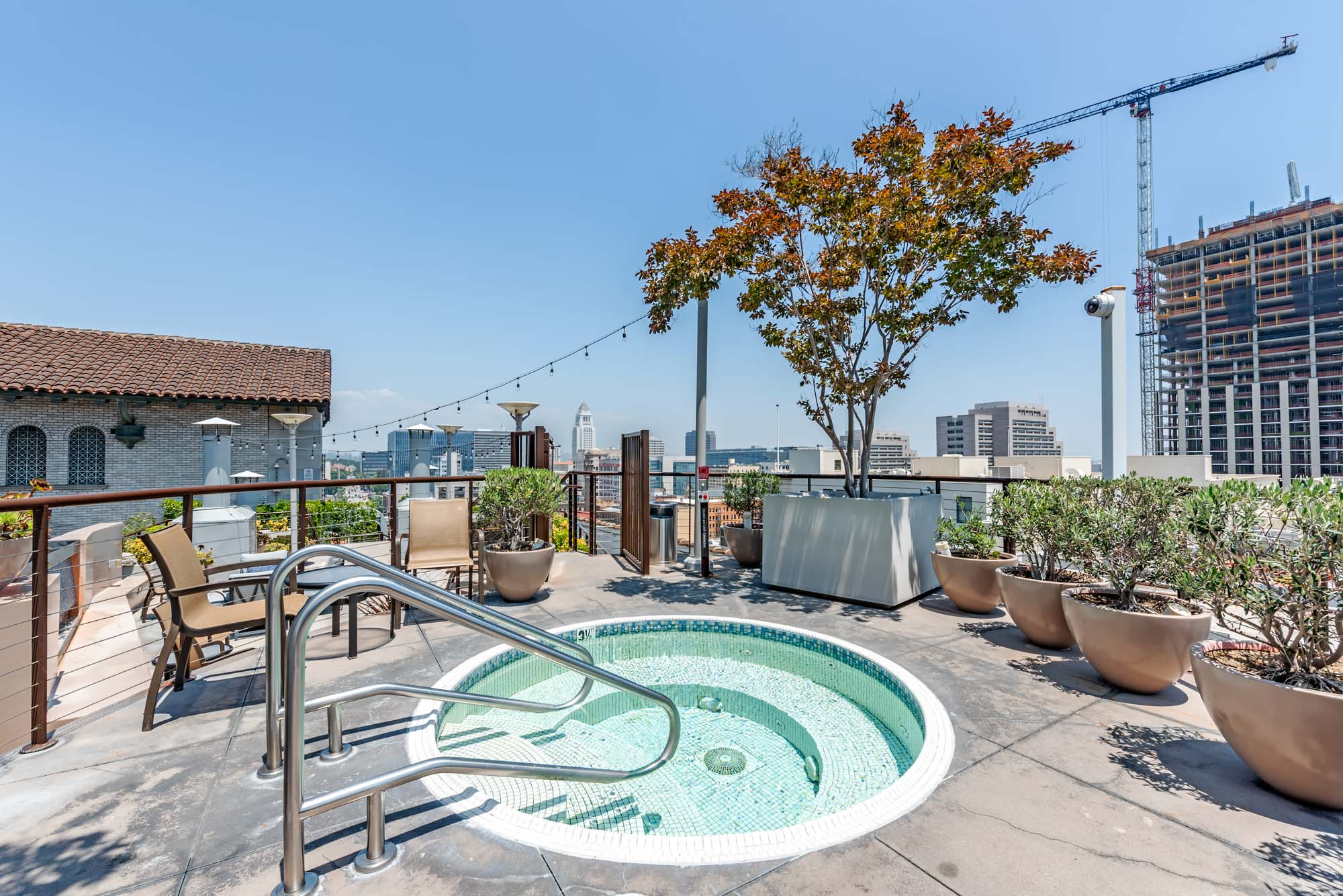A rooftop jacuzzi surrounded by outdoor chairs and pot plants, and a view of the city at Metro 417's apartments in downtown LA