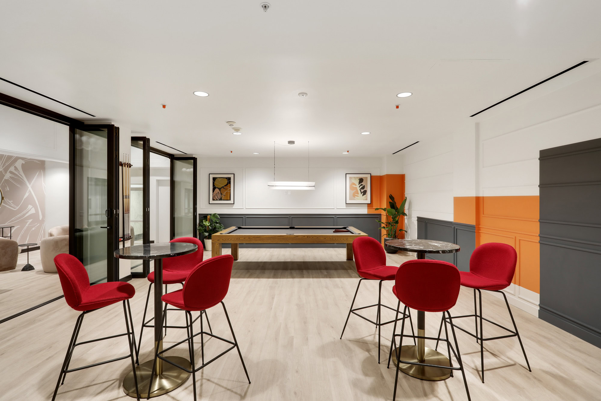 A game lounge with high tables, a pool table and geometrics orange and gray shapes painted on the wall at Metro 417 apartments in DTLA