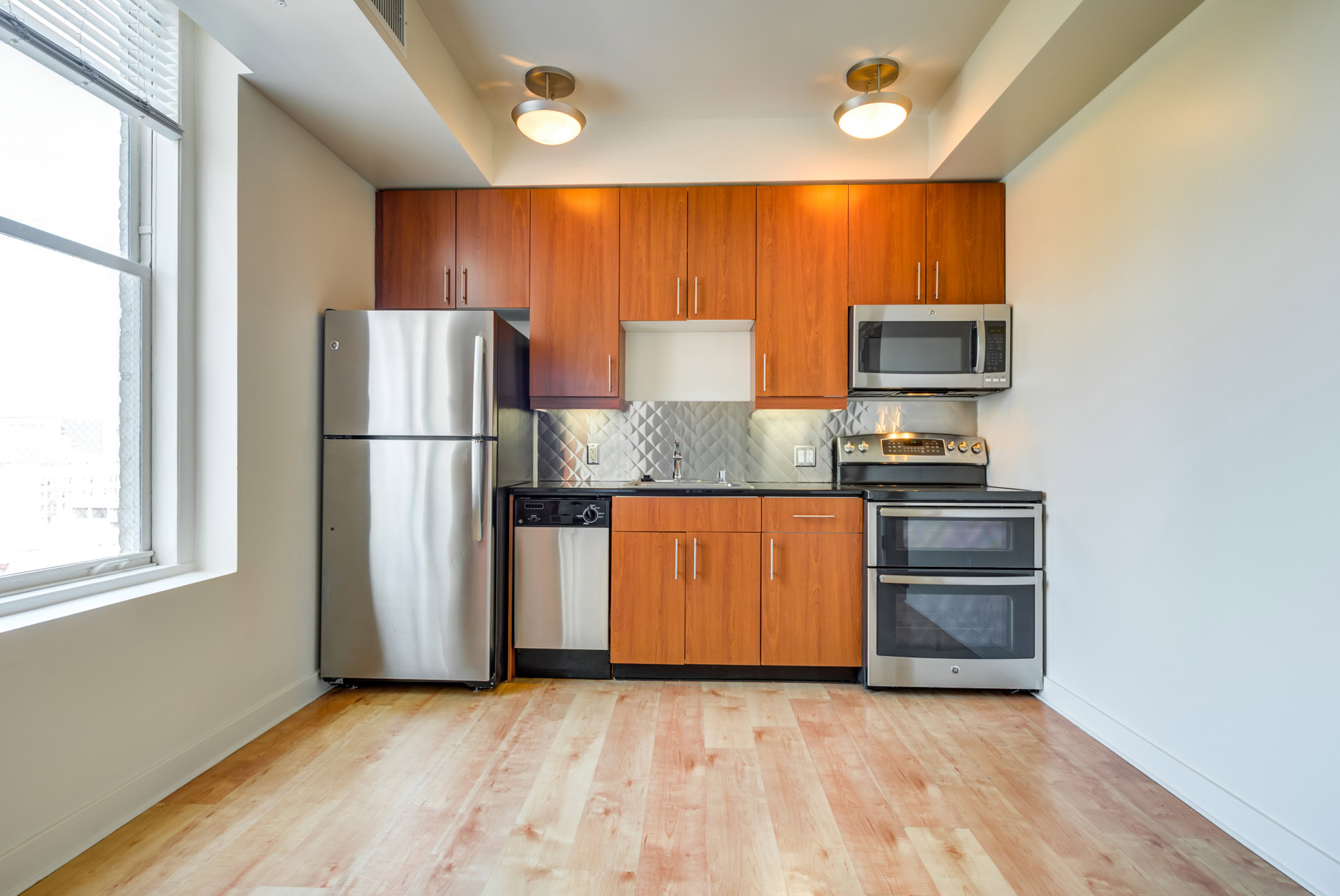 A kitchen with a window, brown cabinets and stainless steel appliances in a Metro 417 apartment in downtown LA