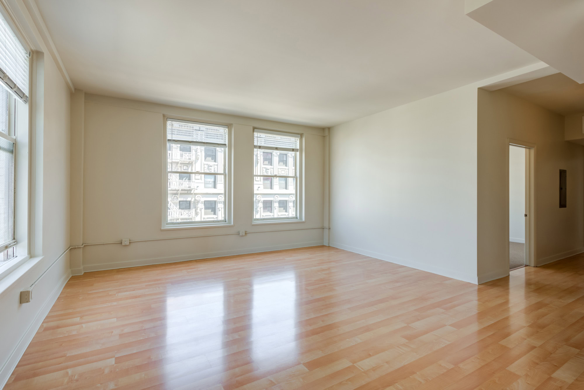 An unfurnished open plan living room and dining area with three windows and a halway to the bedrooms at Metro 417's modern apartments in DTLA