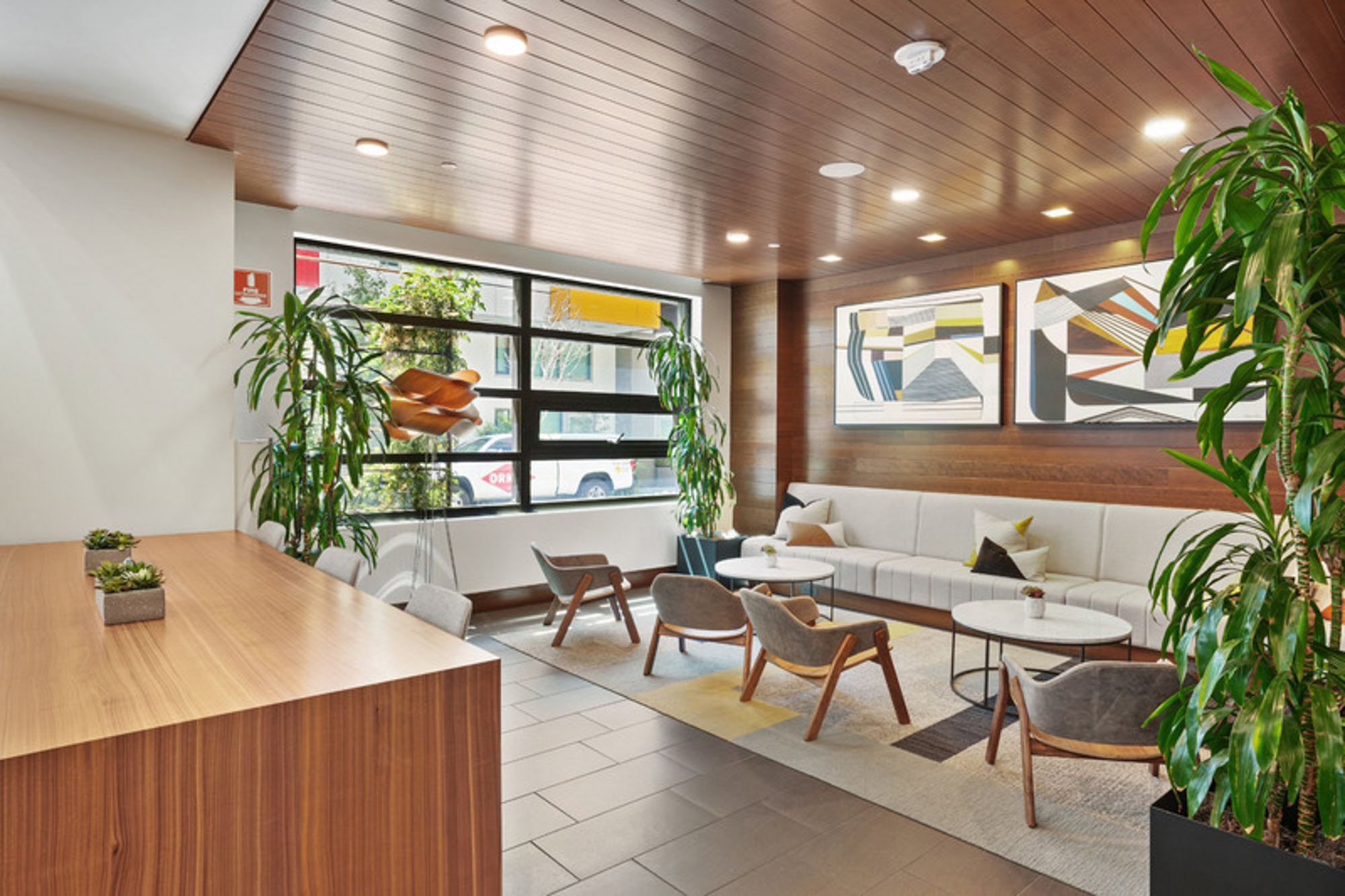 A lobby with booth seating and chairs, tall plants and wood panel ceilings at the Mosso apartments in downtown San Francisco