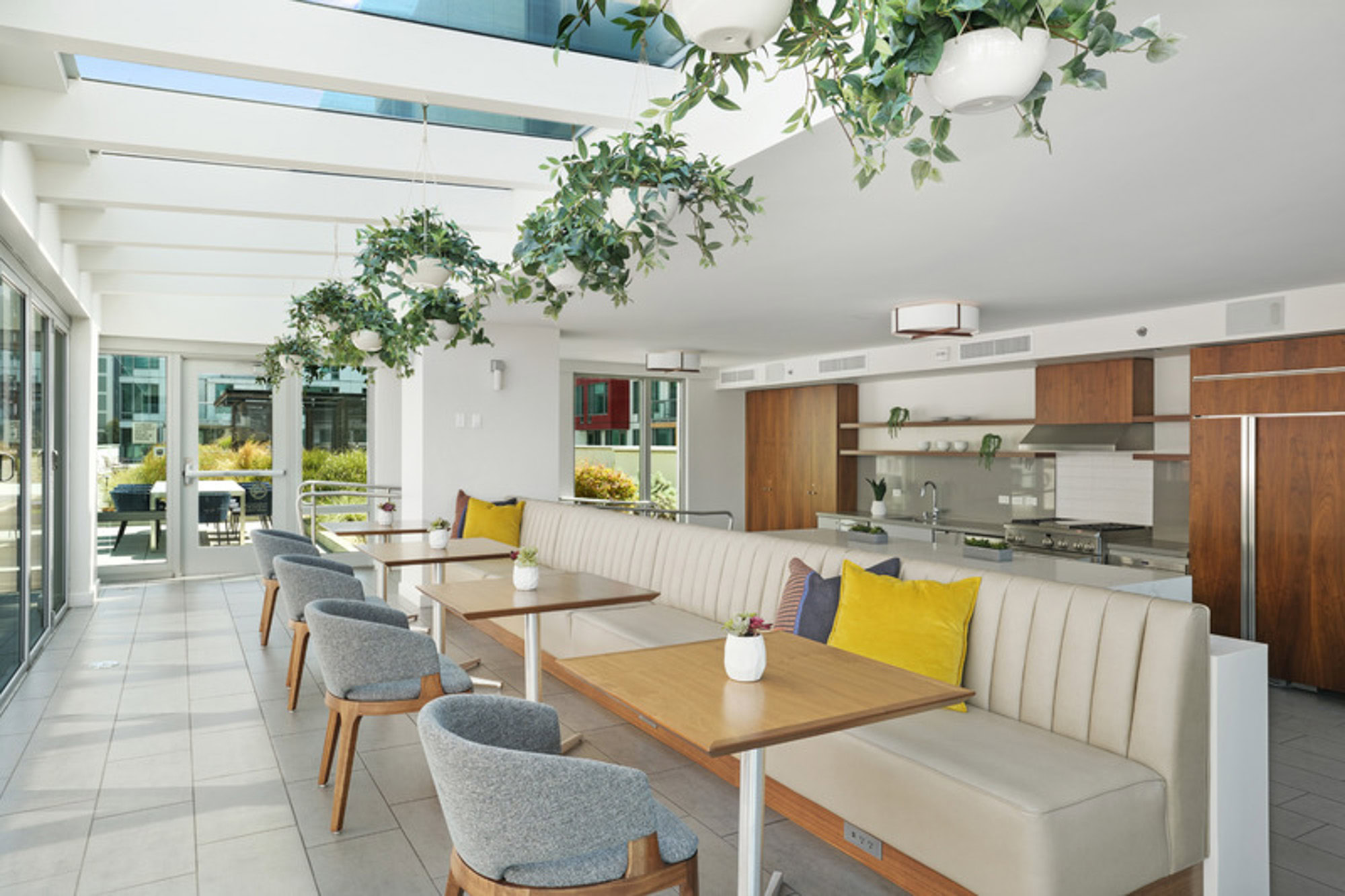 A luxury lounge with leather booth seating and chairs, a kitchen area, glass panel ceilings and overhead plants at the Mosso apartments in downtown San Francisco