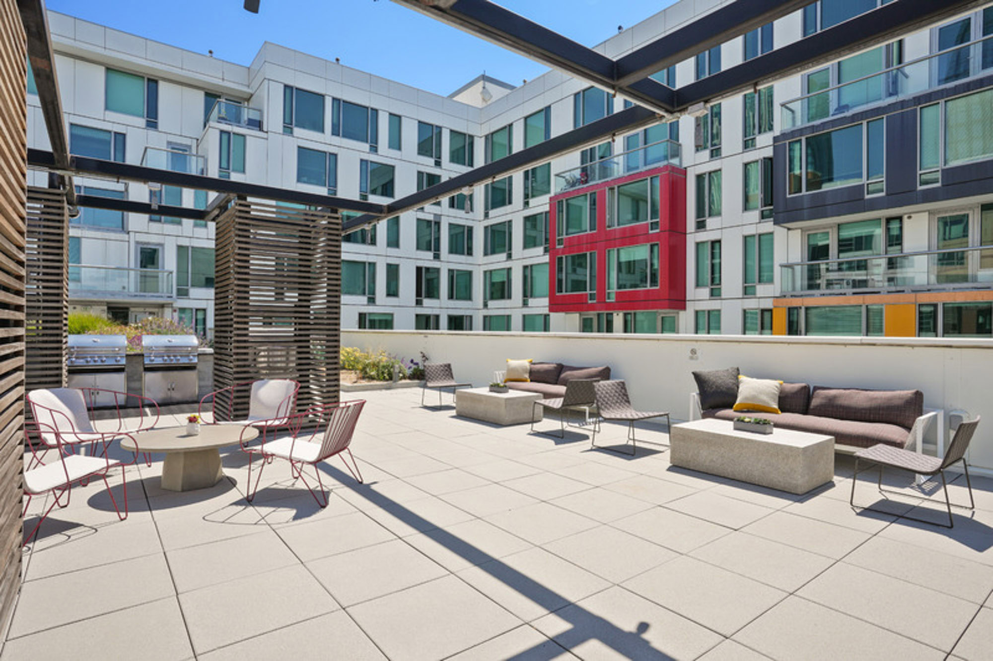 A mid-level, outdoor terrace with lounging chairs, couches and grills surrounded by the Mosso luxury apartments in San Francisco