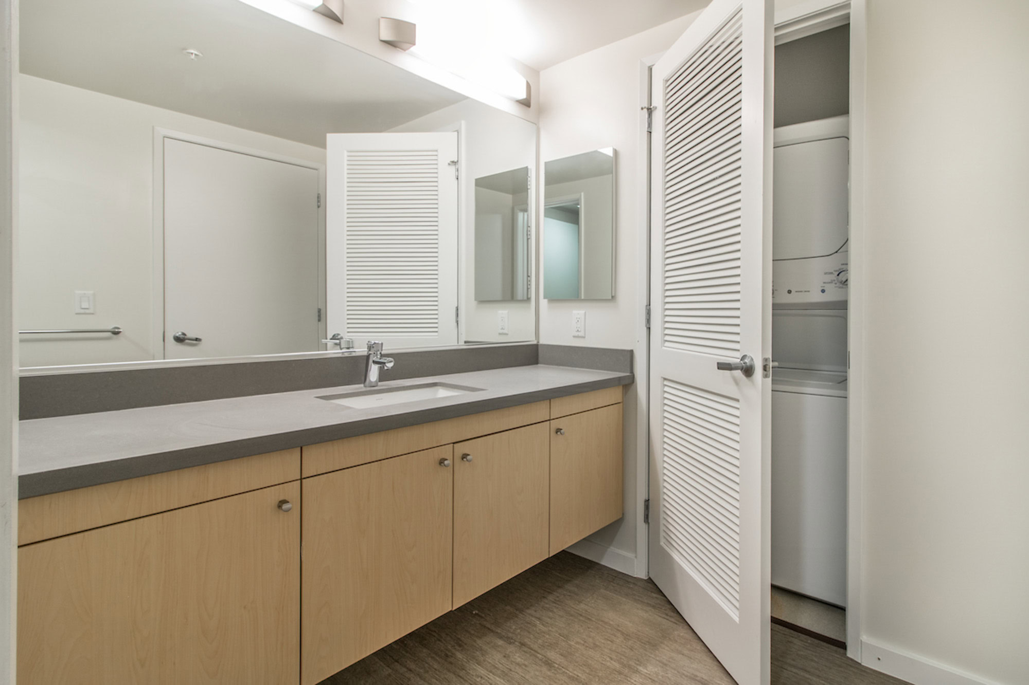 A spacious bathroom with a long sink counter and an in unit stacked washer and dryer at Mosso apartments in San Francisco