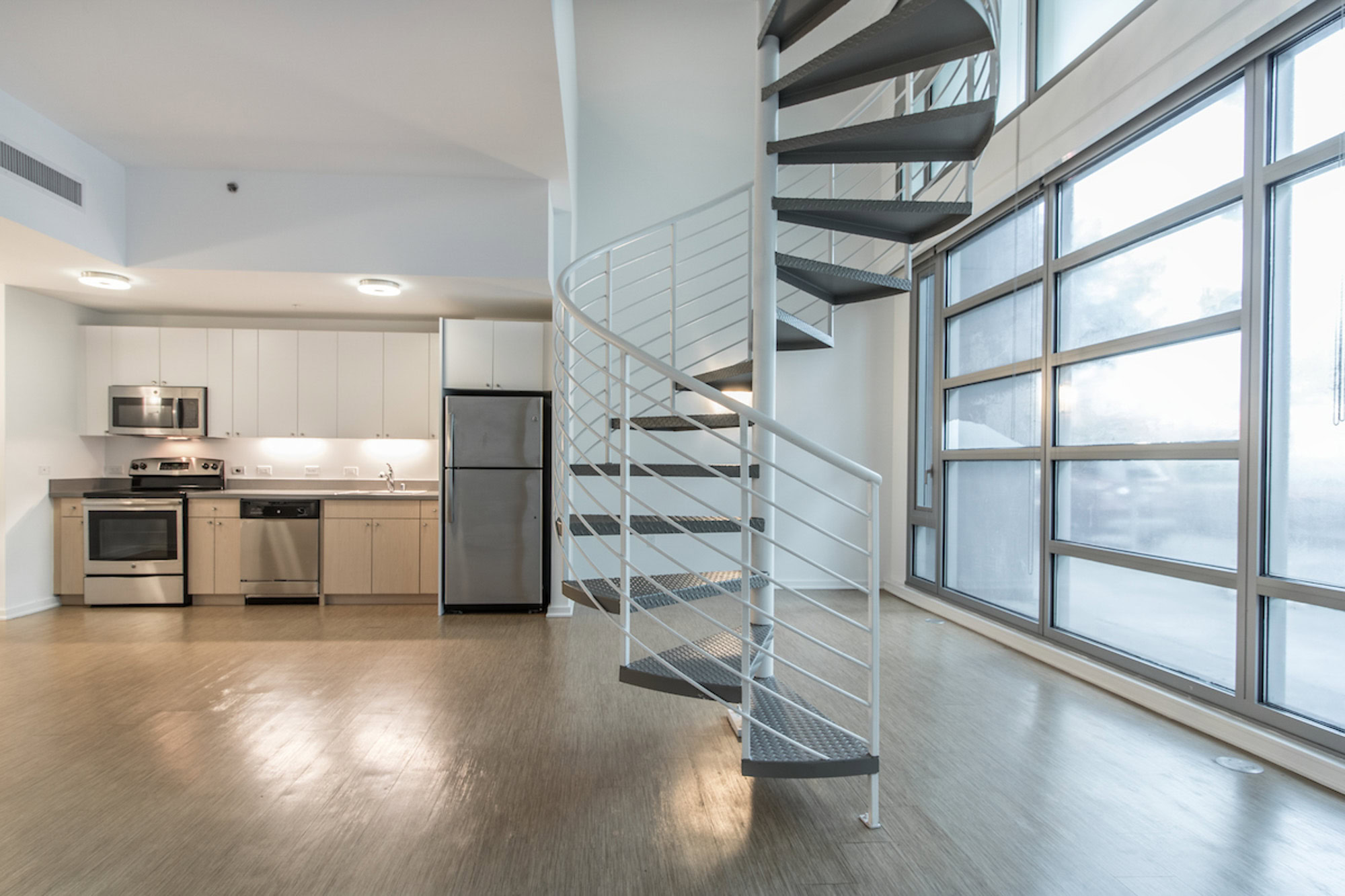 An empty open plan apartment living room and kitchen with a spiral staircase and a frosted glass window wall at Mosso apartments in San Francisco