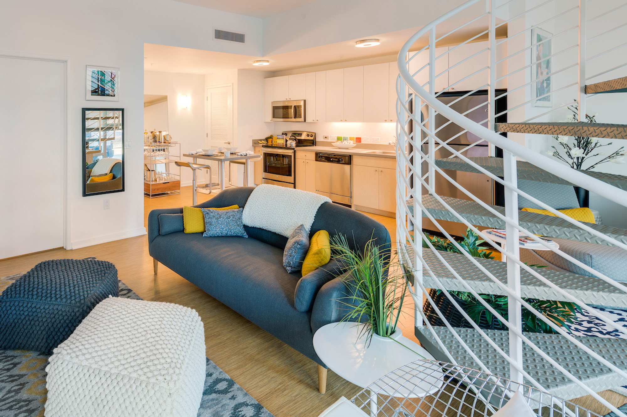 An open plan living room with a kitchen behind it and a spiral staircase at Mosso apartments in San Francisco