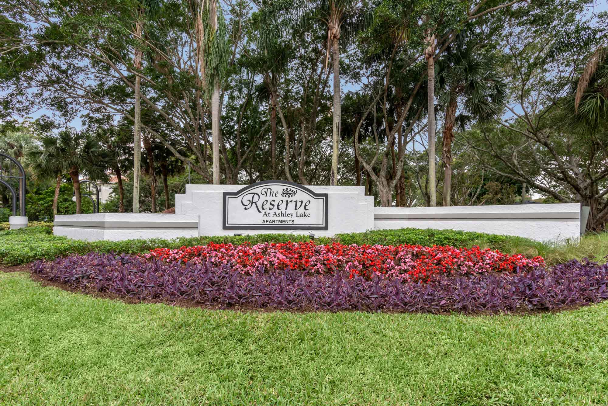 A sign that says 'The Reserve at Ashley Lake' with flowers in front of it at the entrance of the apartments for rent in Boynon Beach