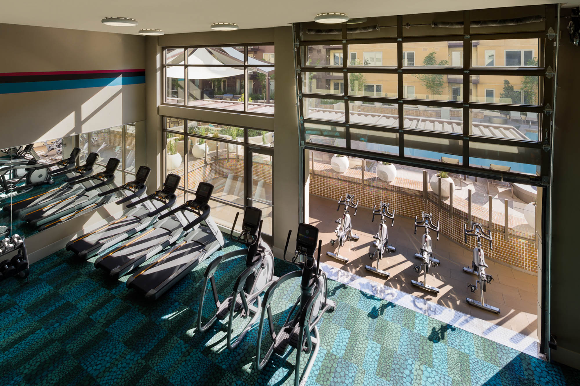 A state of the art gym with rows of stationary bikes, treadmills and ellipticals overlooking the pool courtyard at The Village Residences new Mountain View apartments