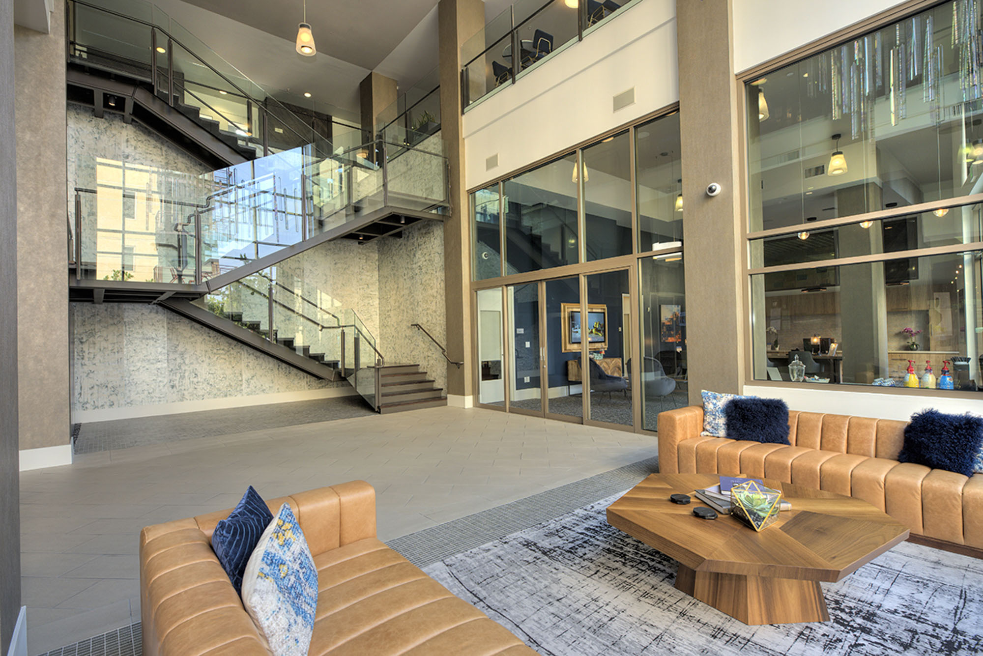 A lobby lounge with glass doors to leasing offices and stairs to coworking spaces at The Village Residences new apartments in Mountain View CA
