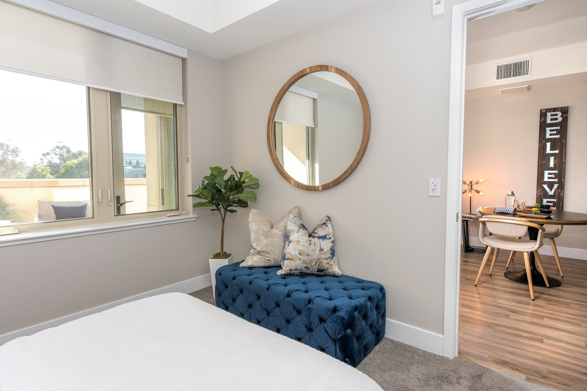 A bedroom with a large window and carpet flooring, facing the living room area at The Village Residences new apartments in Mountain View, CA