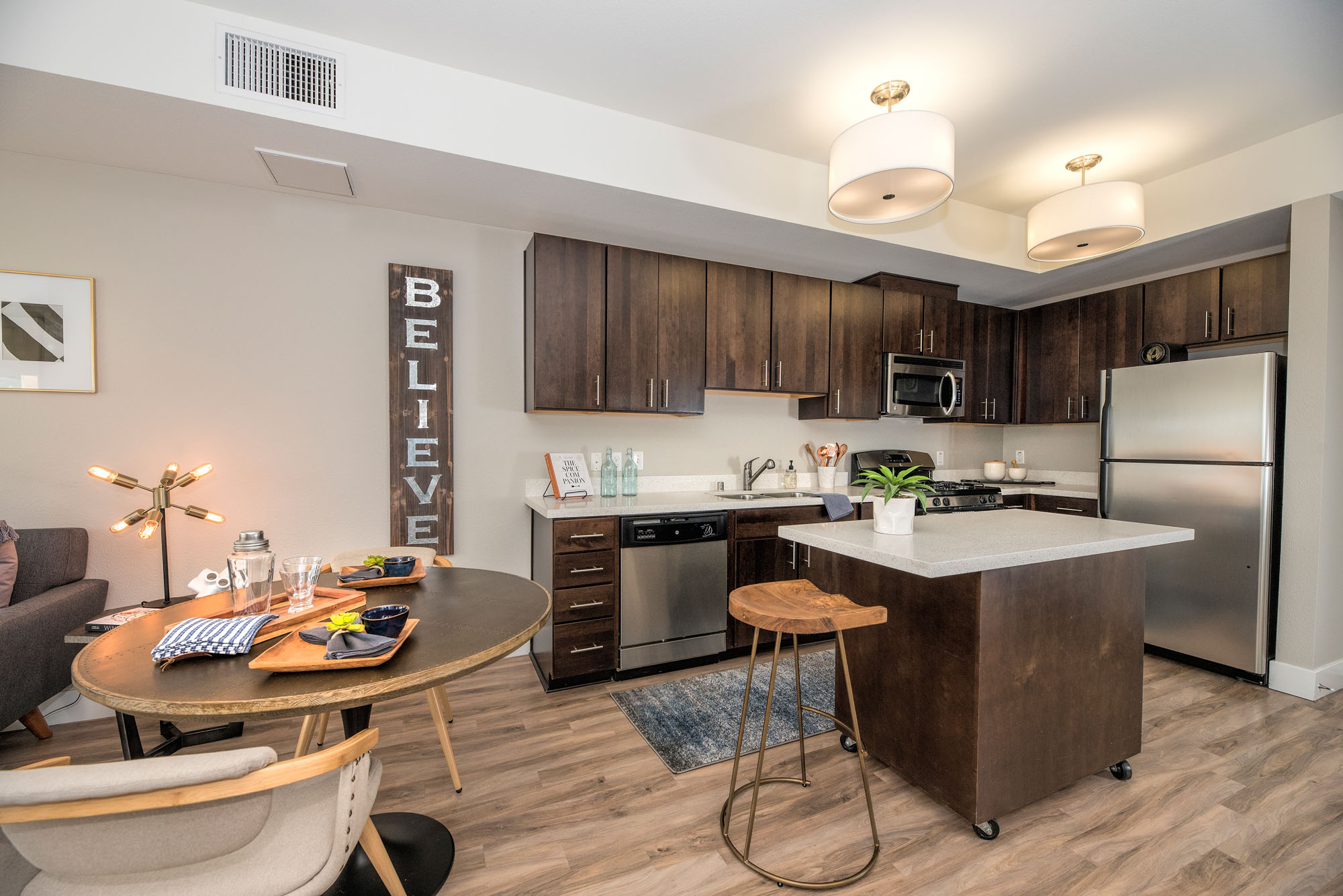 A dining area and kitchen with hardwood floors, brown cabinets and a movable kitchen island at The Village Residences new apartments in Mountain View, CA