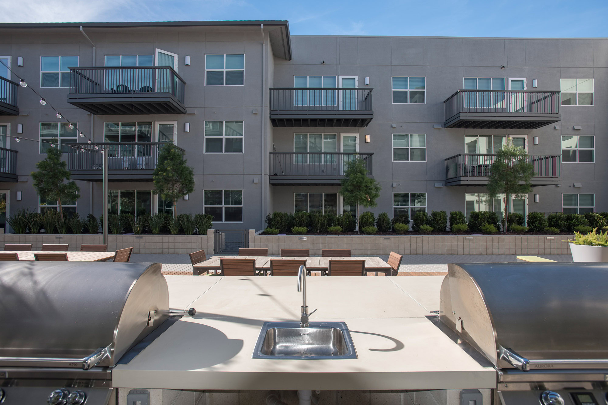 A grilling station next to dining tables in a courtyard overlooked by surrounding apartments in Vintage luxury apartments in Pleasanton, CA