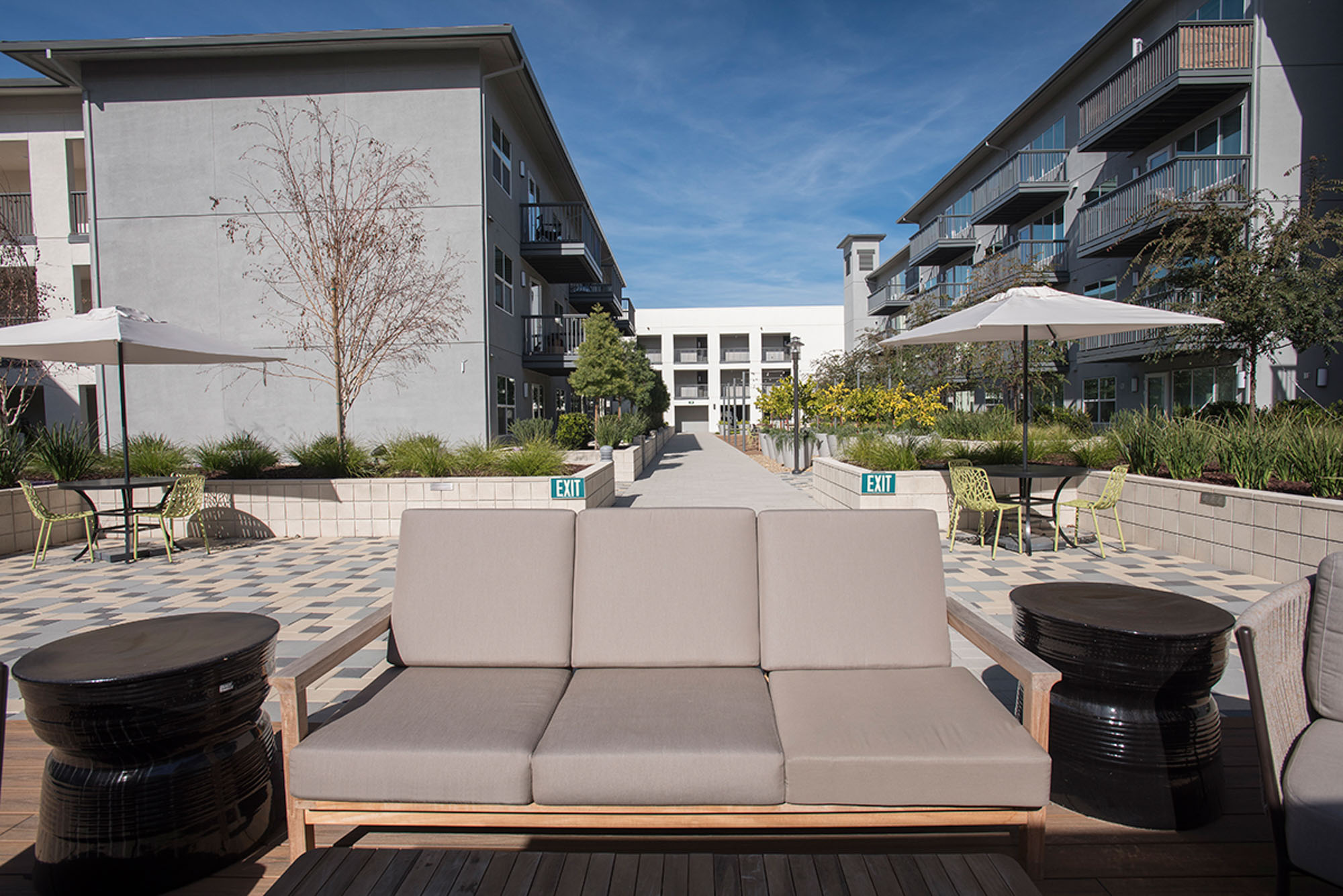 An outdoor couch with outdoor eating spaces with umbrellas in the courtyard of the Vintage apartments in Pleasanton, CA