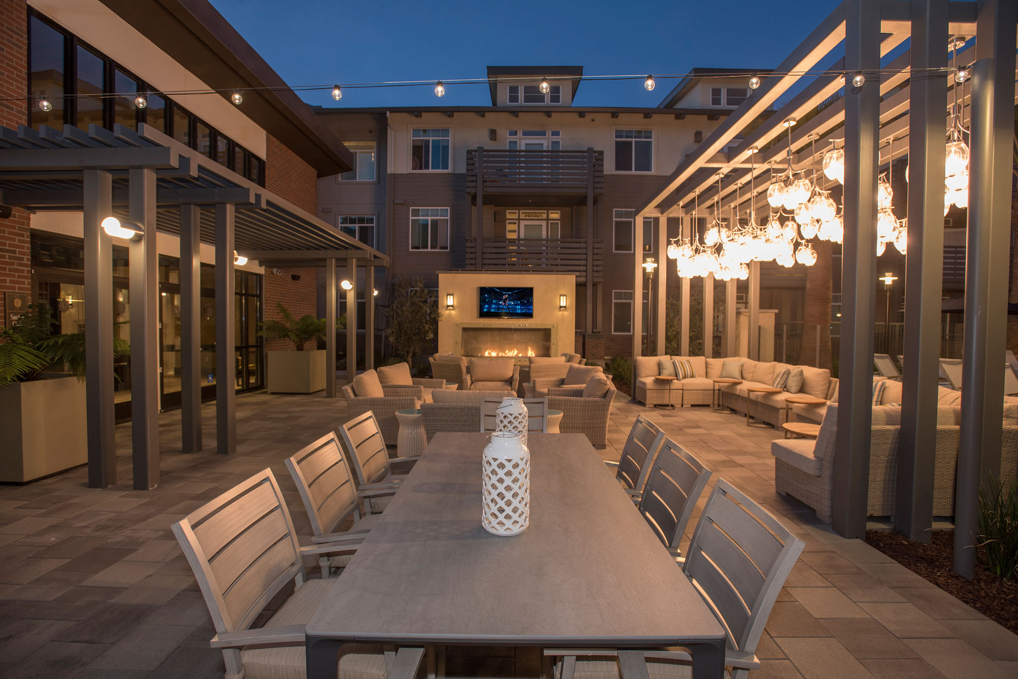 An outdoor terrace with dining tables and lounge seating areas, outdoor hanging lights and a fireplace at the Vintage apartments in Pleasanton, CA
