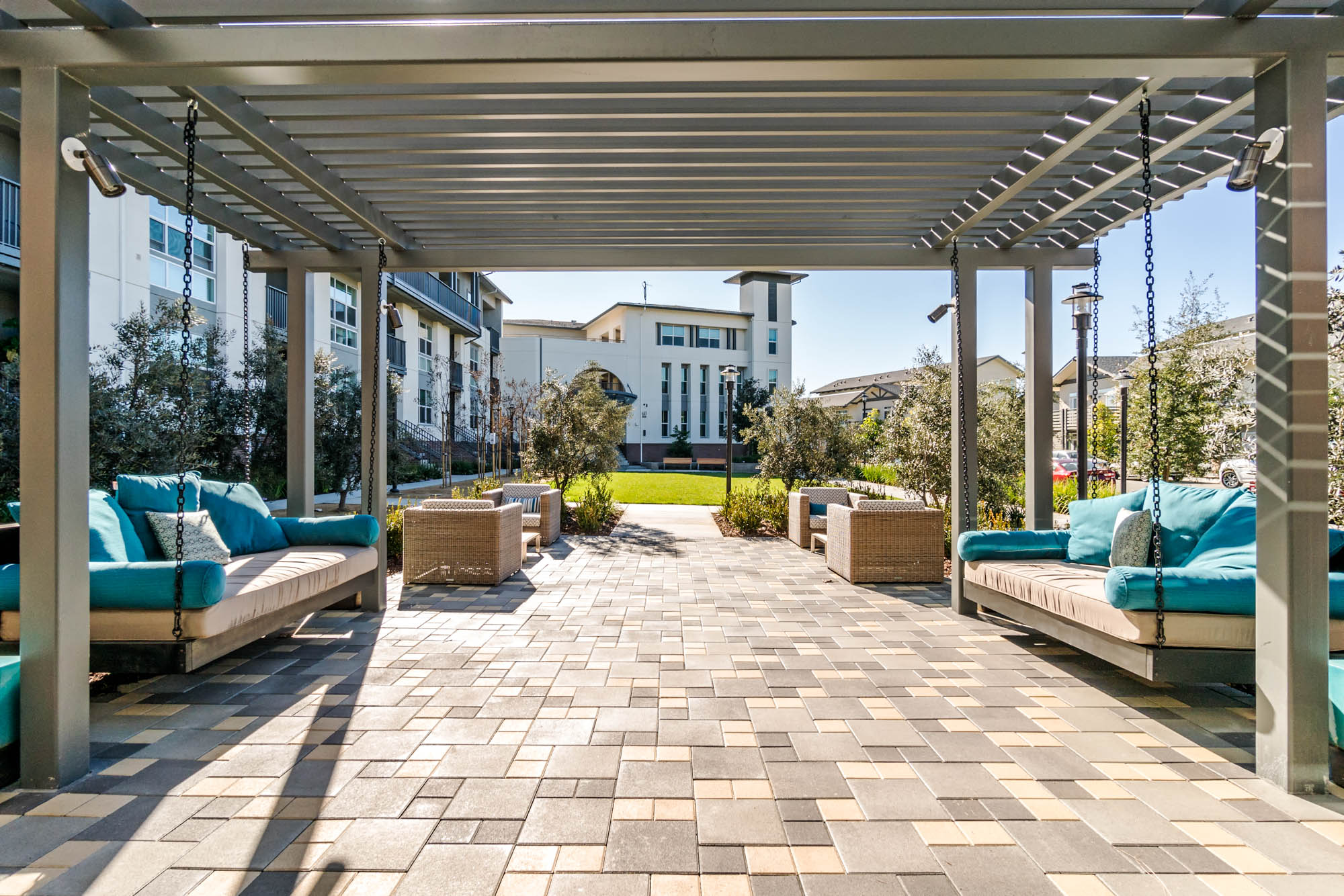 An outdoor lounge on a spacious walkway from sliding doors partially covered by a pergola at the Vintage apartments in Pleasanton, CA