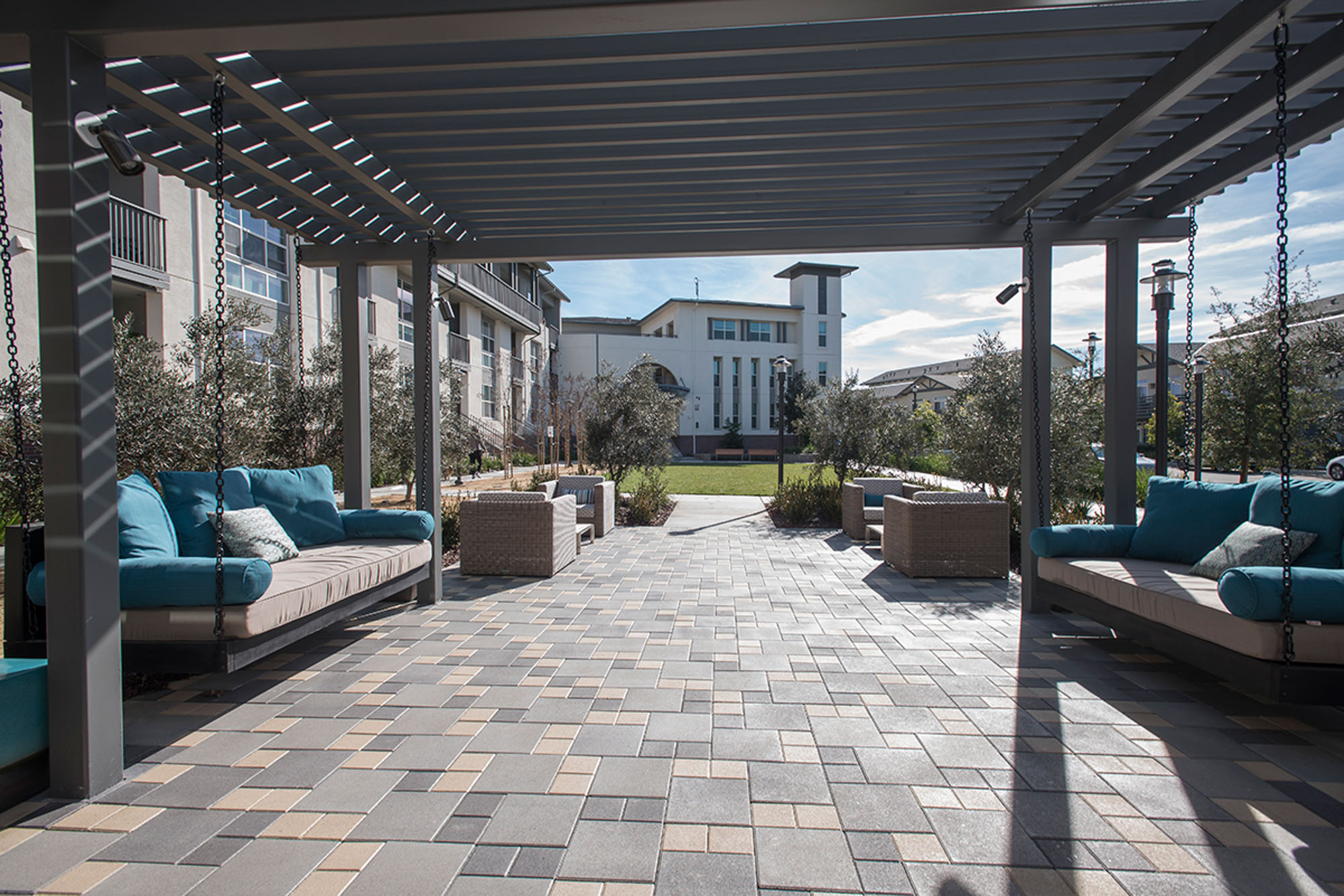 An outdoor lounge on a spacious walkway from sliding doors partially covered by a pergola at the Vintage apartments in Pleasanton, CA