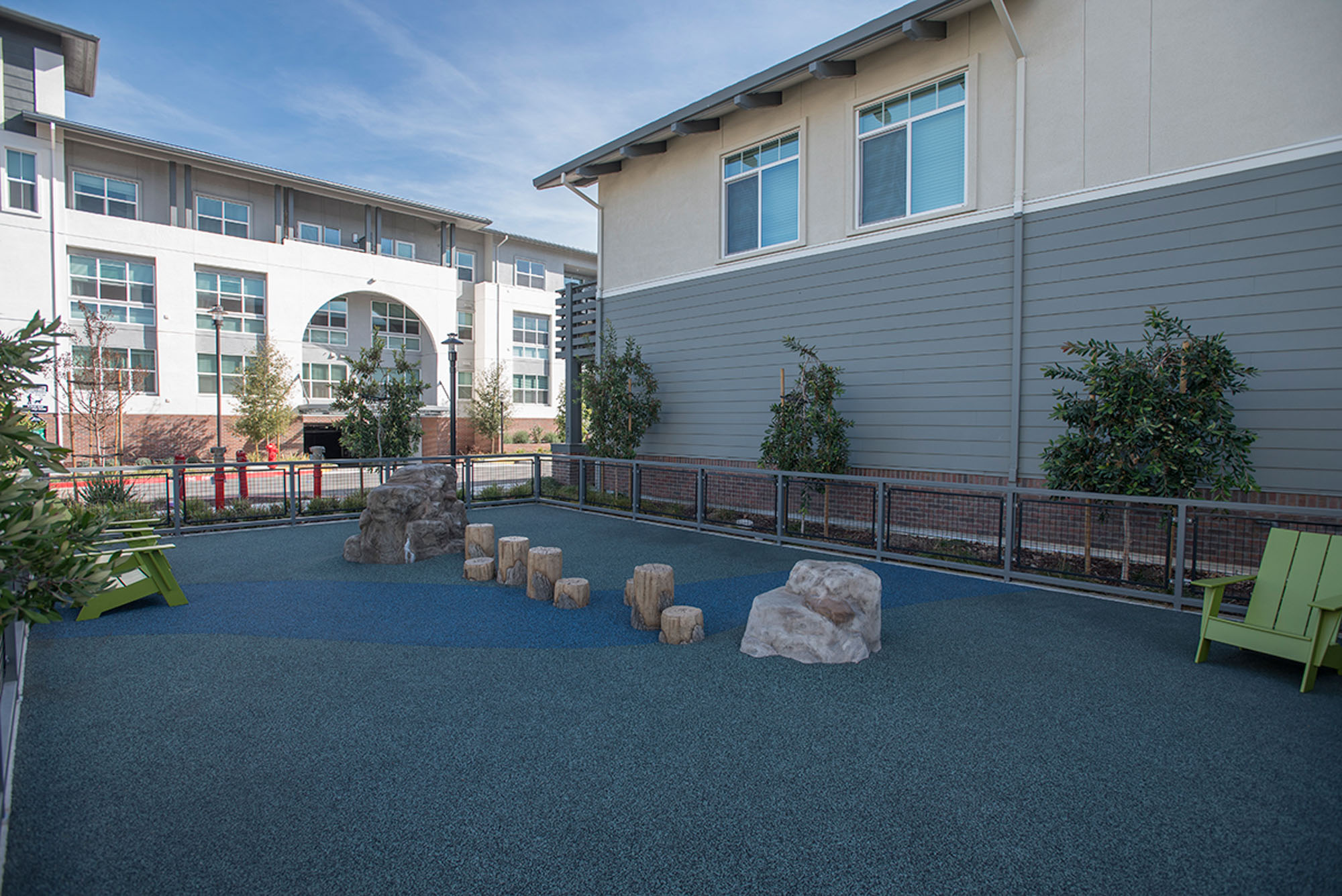 A gated playpen with fake rocks, stepping logs and outdoor lounge chairs at the Vintage apartments in Pleasanton, CA