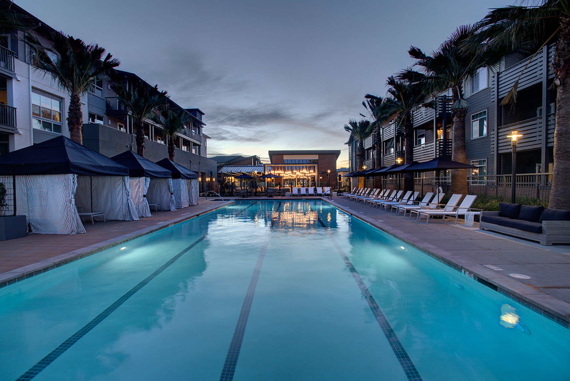 A pool with four lanes, and lounging chairs and cabanas on either side at the Vintage luxury apartments in Pleasanton, CA