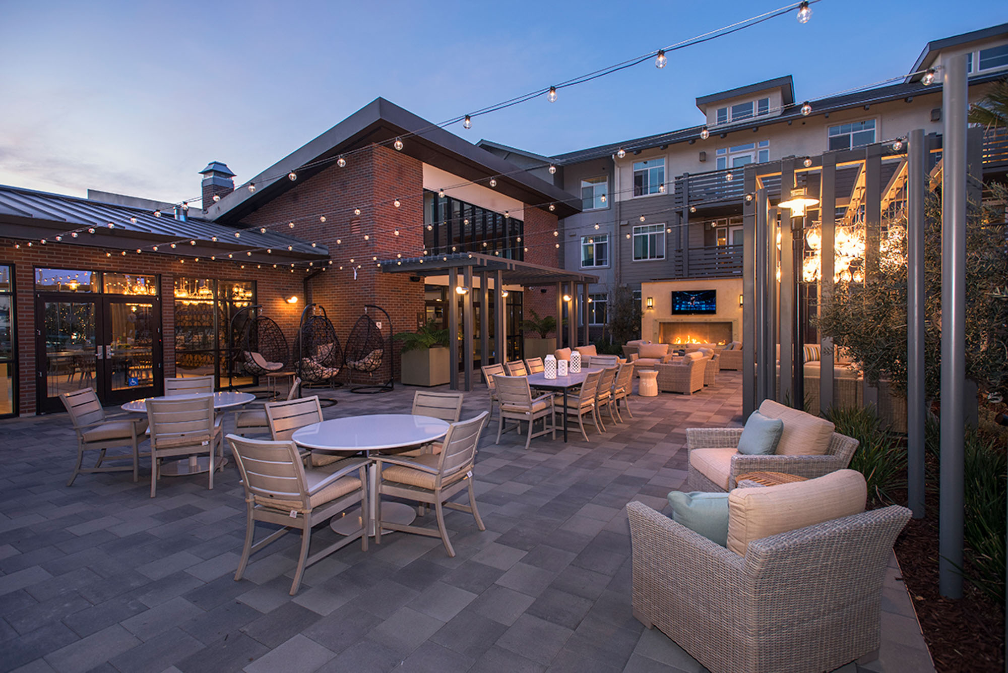An outdoor courtyard with dining tables, lounging chairs and a fire place at the Vintage apartments in Pleasanton, CA