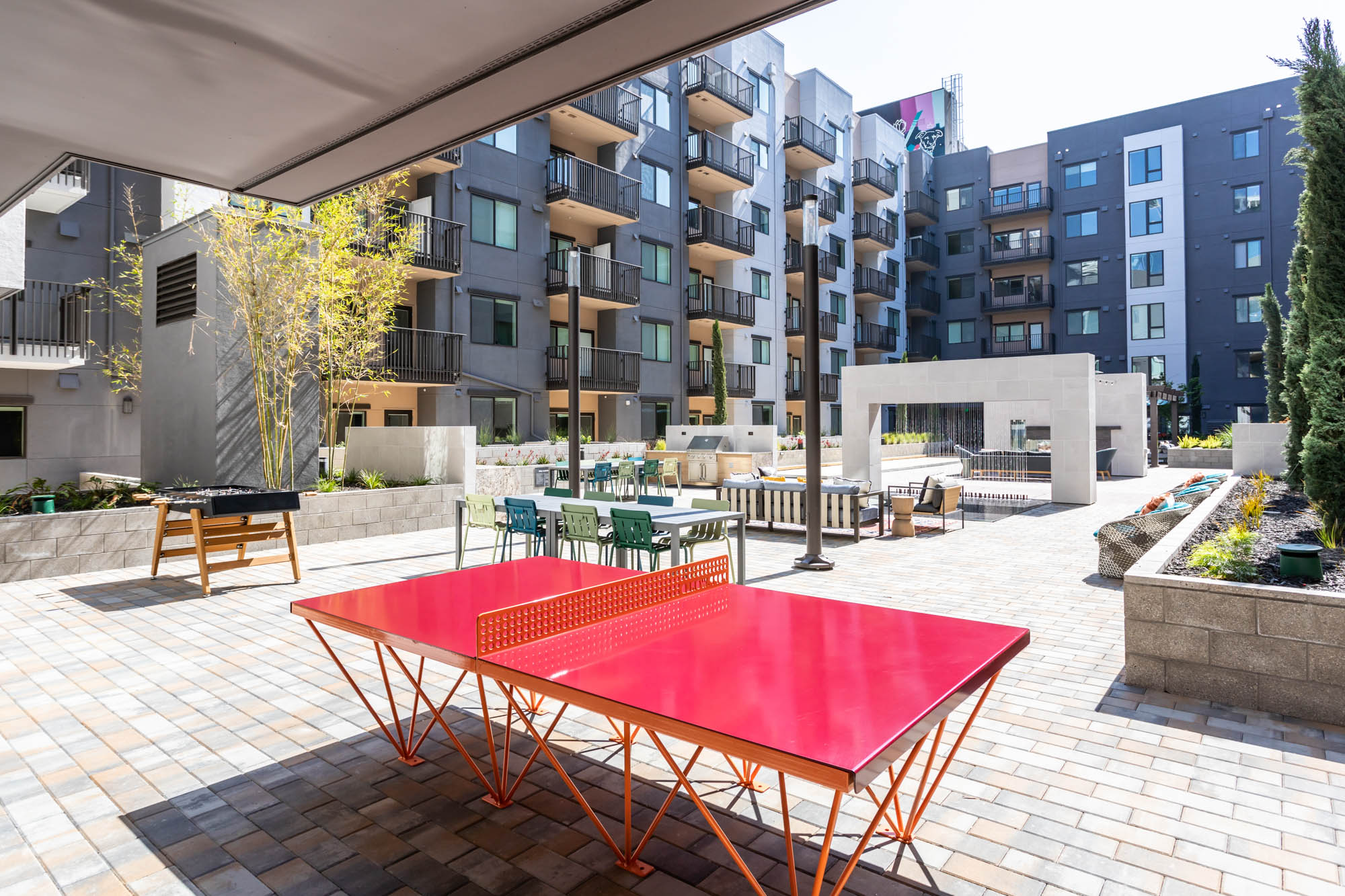 A red ping pong table and foosball in a courtyard with a fountain and dining tables at the Webster Eleven apartments in downtown Oakland