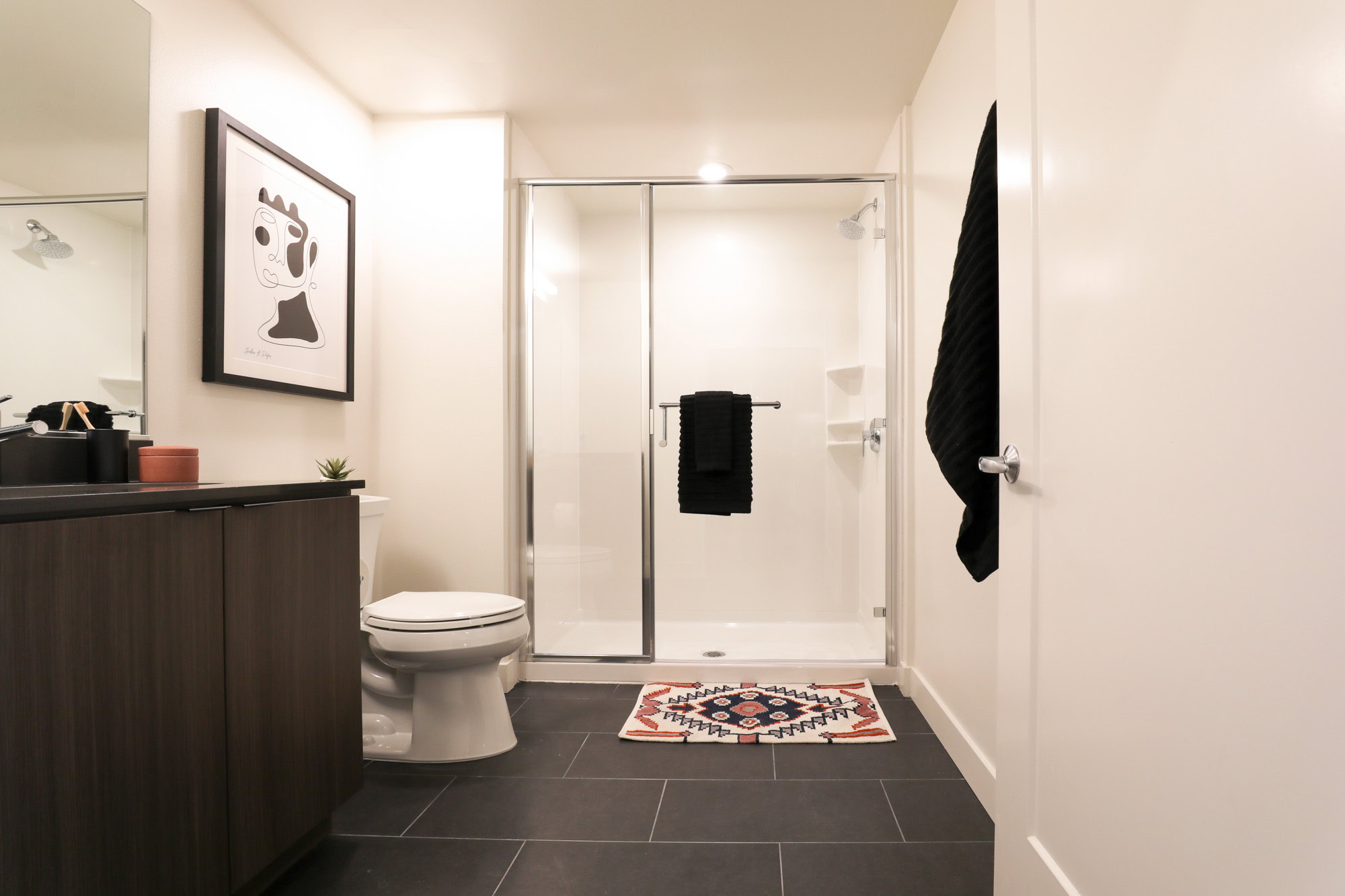 A bathroom with a stand up shower and black tile floors at the Webster Elevens downtown Oakland apartments for rent