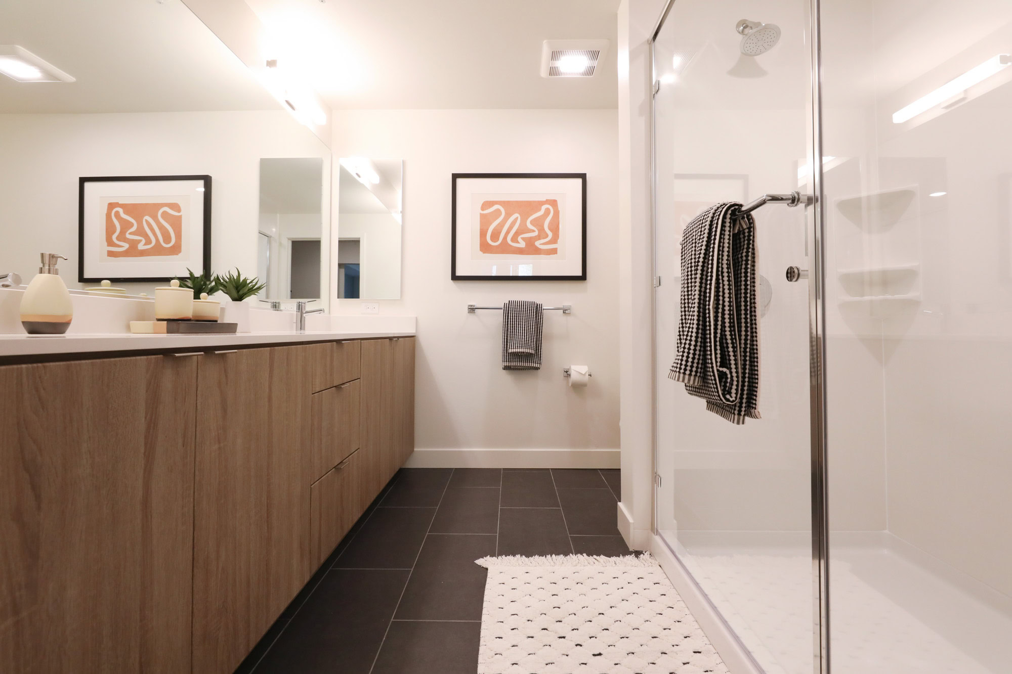 A spa-like bathroom shower and long vanity sink with black tile floors at the Webster Elevents downtown Oakland apartments