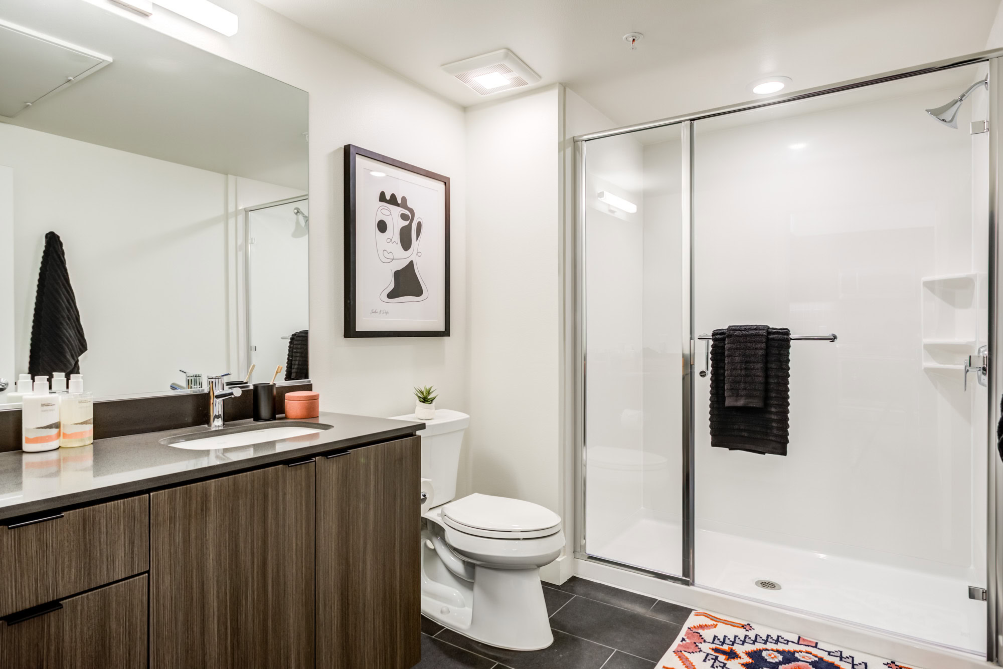 A bathroom with a stand up shower and black tile floors at the Webster Elevens downtown Oakland apartments for rent